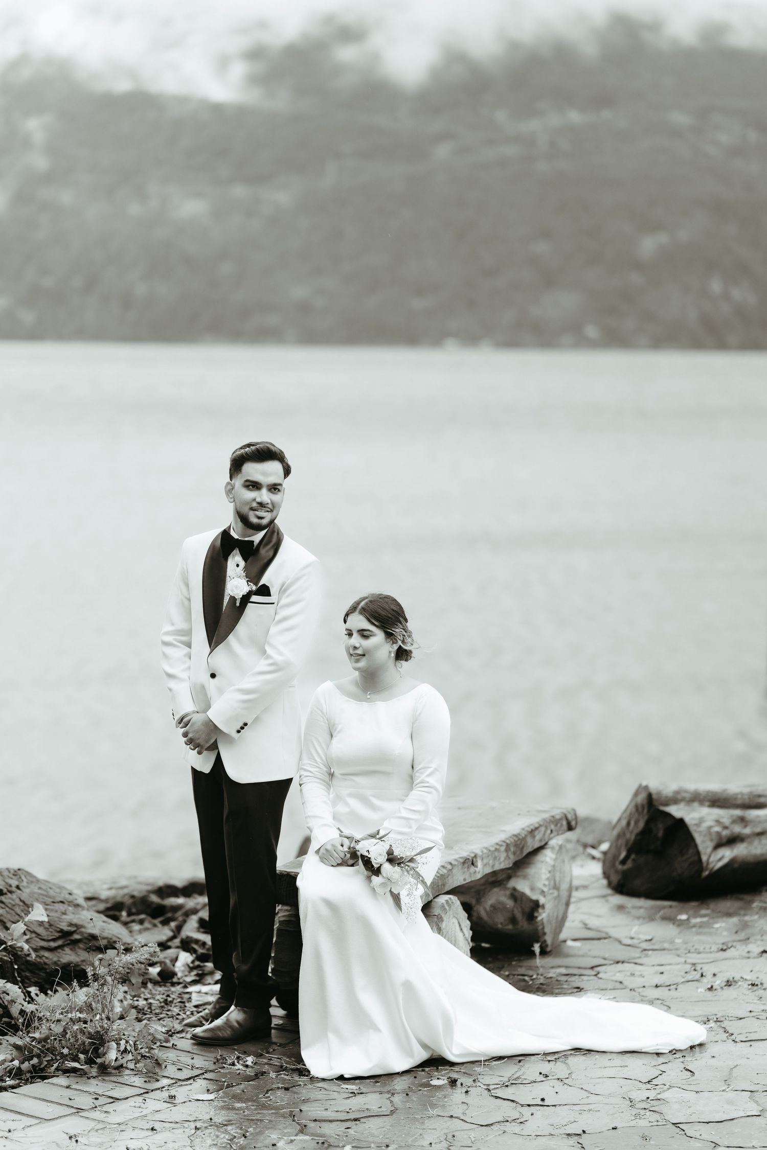 A vintage black and white wedding photo sequence showing a couple sitting together on rocks by a lake.
