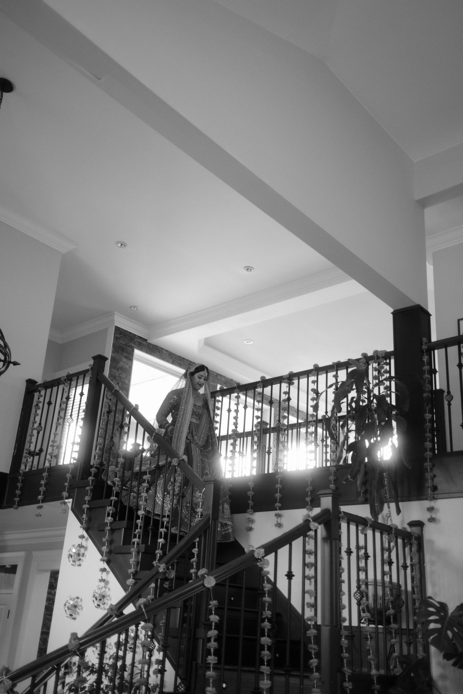 Black and white photo of a woman posing on an ornate staircase with decorative iron railings in an elegant interior.