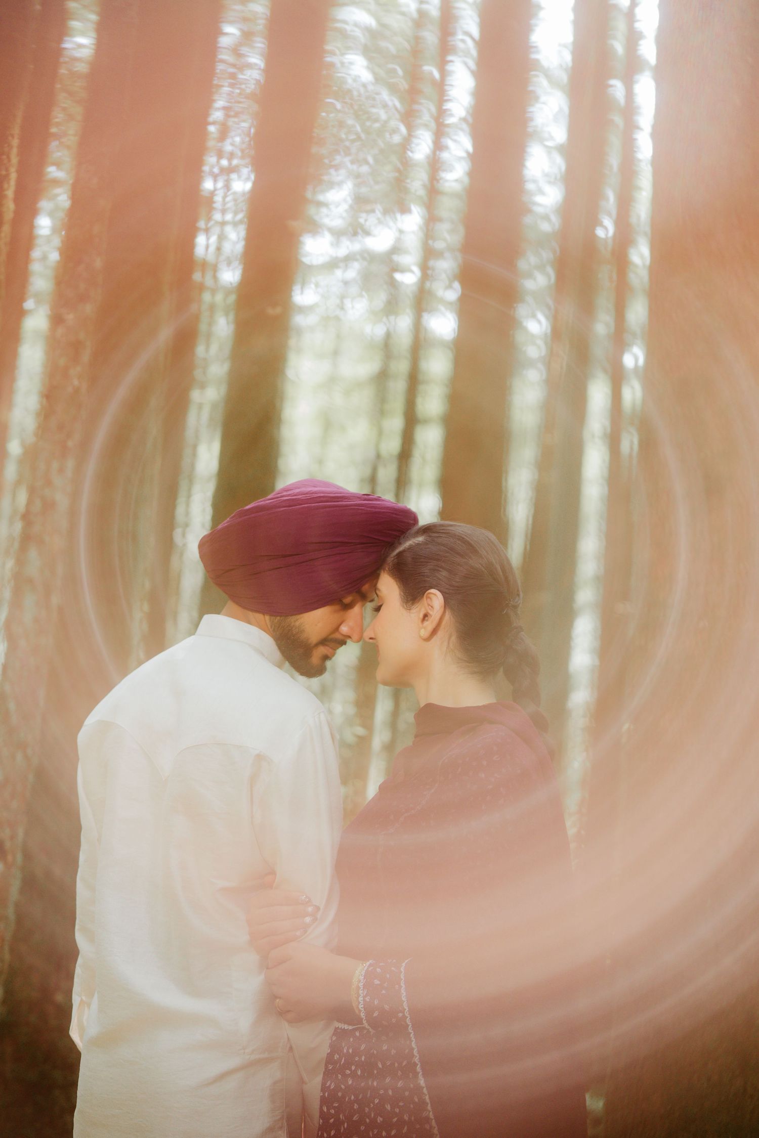 Sikh couple sharing an intimate moment in forest with dreamy lens flare effect.