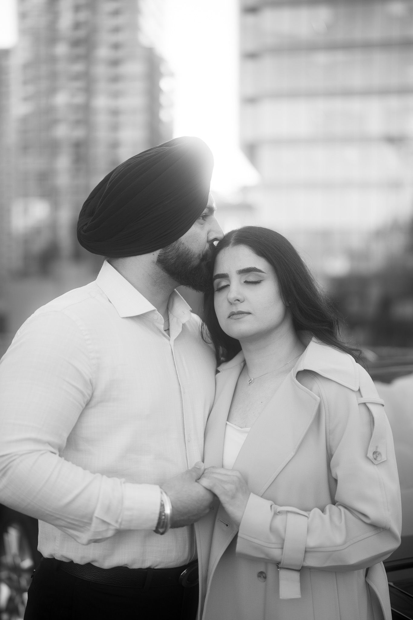 A romantic black and white portrait of a couple embracing outdoors in an urban setting.