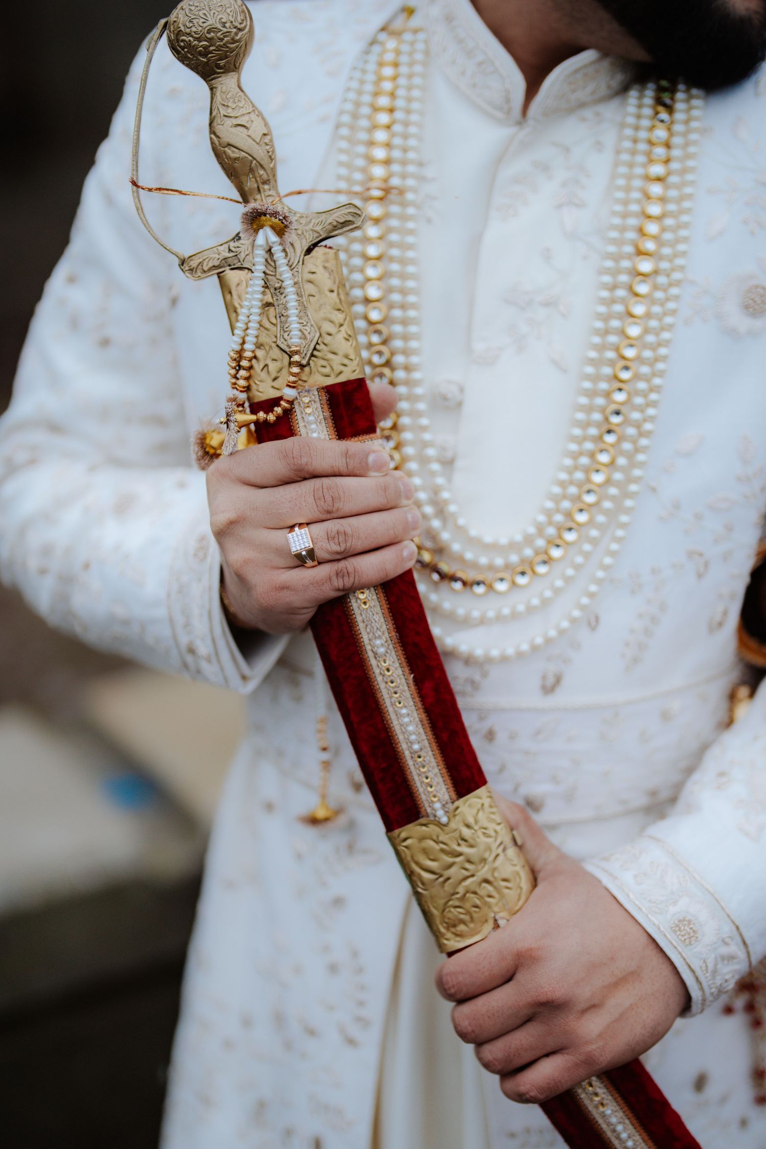 Close-up details of ceremonial sword with ornate gold handle against white traditional dress.