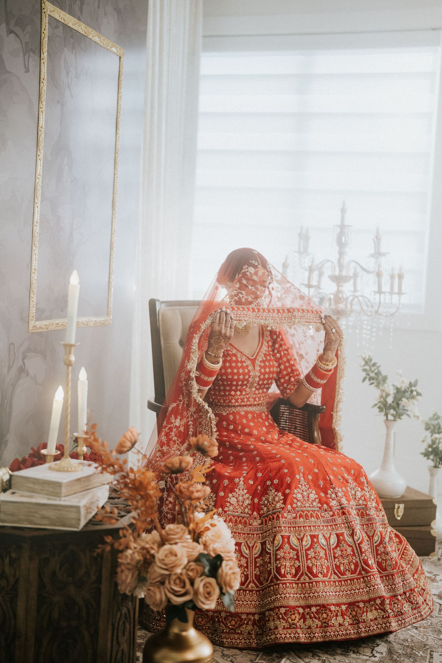 Traditional Indian bridal photoshoot in red lehenga with elegant room decor and roses.