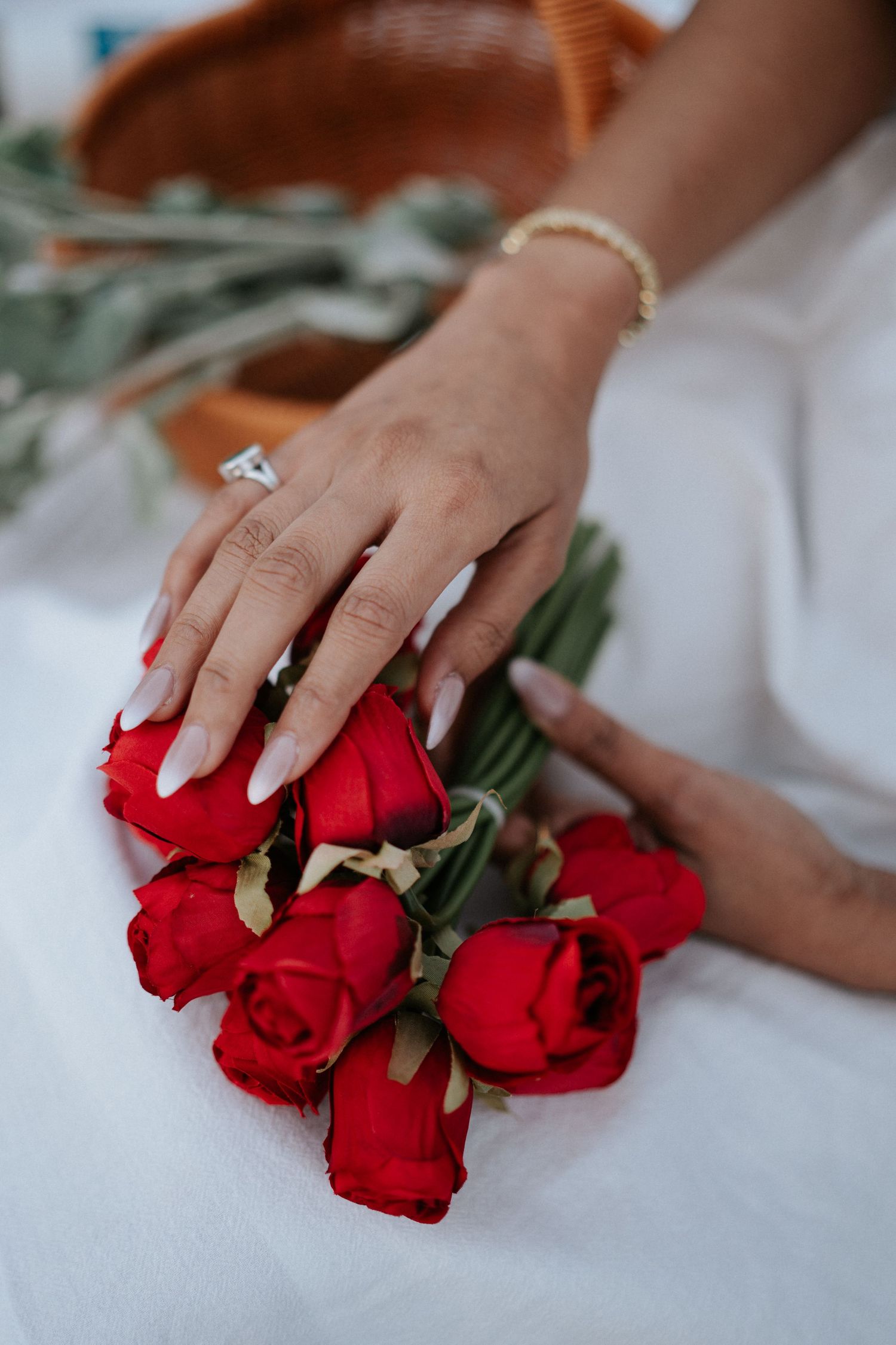 Hands arranging fresh red roses on white surface with engagement ring visible.