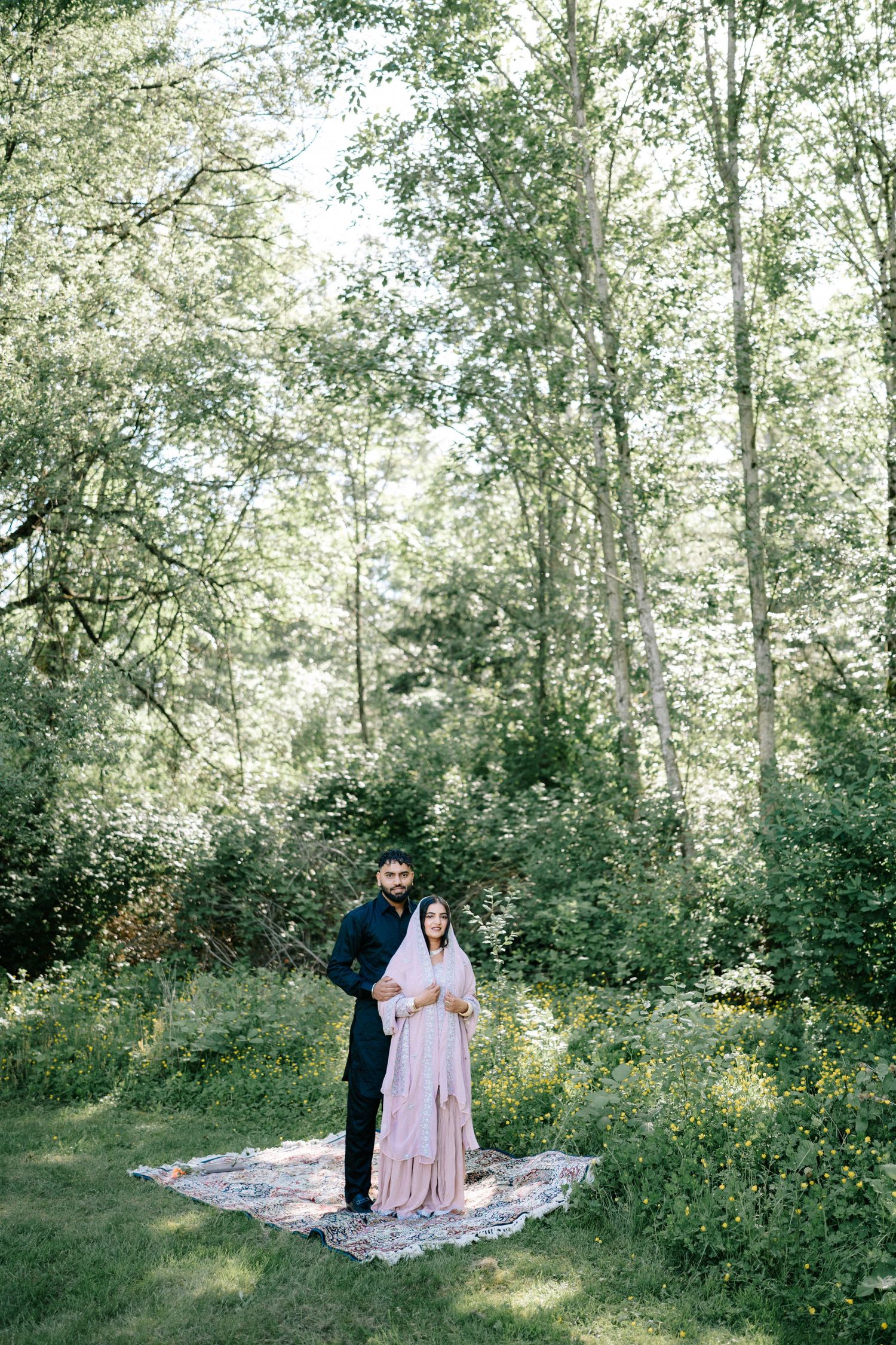 Couple shares romantic moment on blanket in sunlit forest clearing.