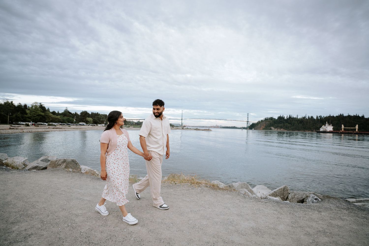 Two people in matching white attire dance together on a scenic coastal shoreline.