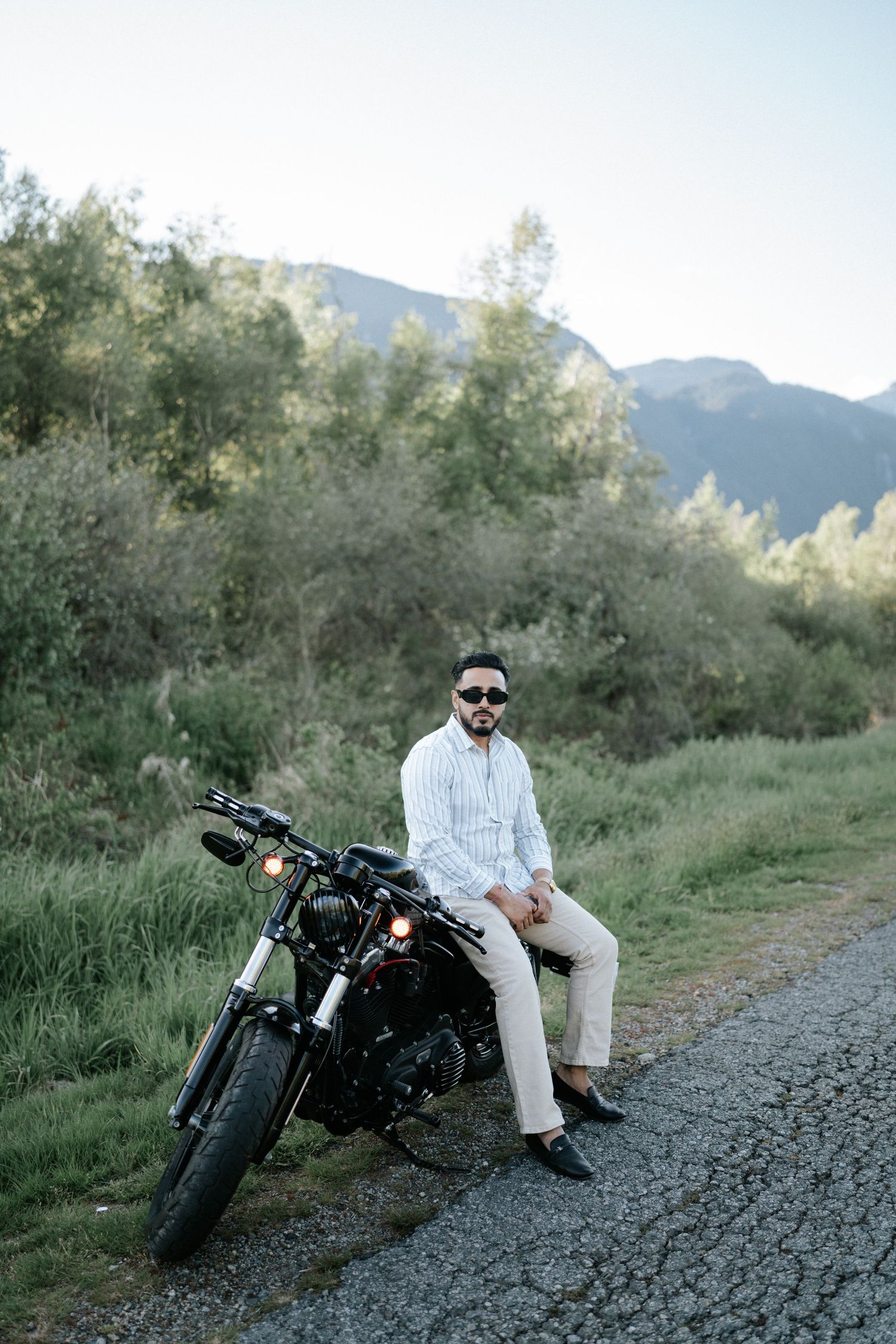 A motorcycle parked on a gravel path with mountains and trees in the background during golden hour.