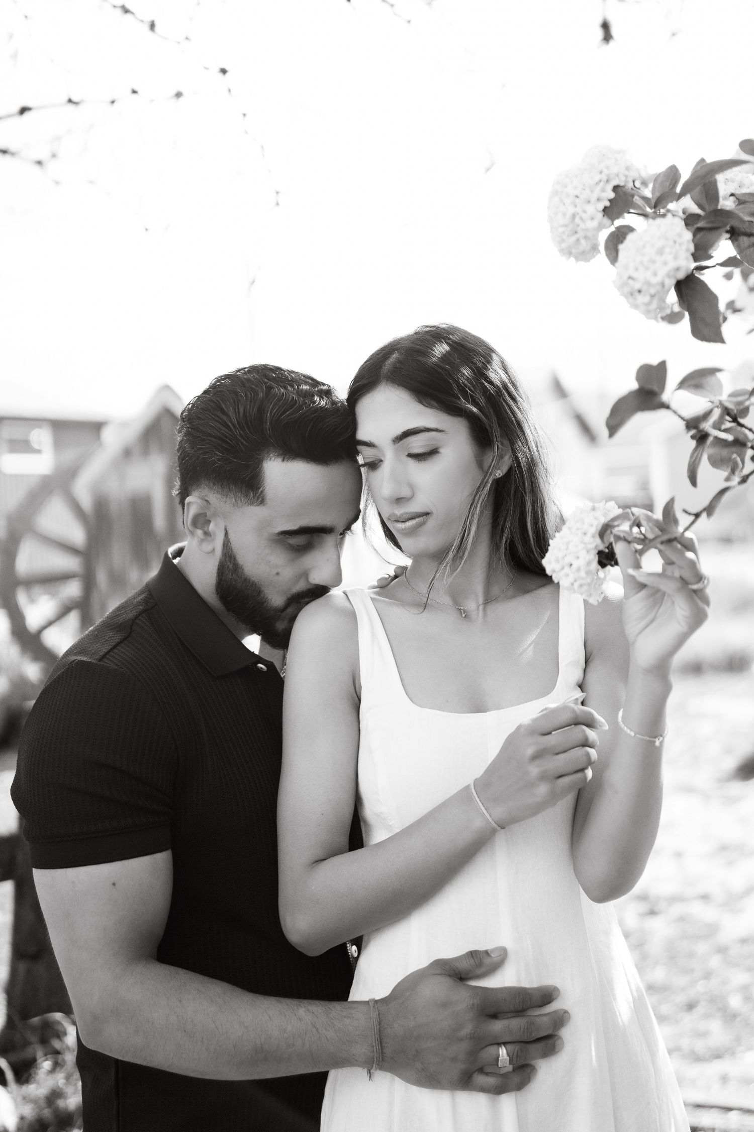A romantic black and white portrait of a couple embracing outdoors with delicate flowers in the foreground.
