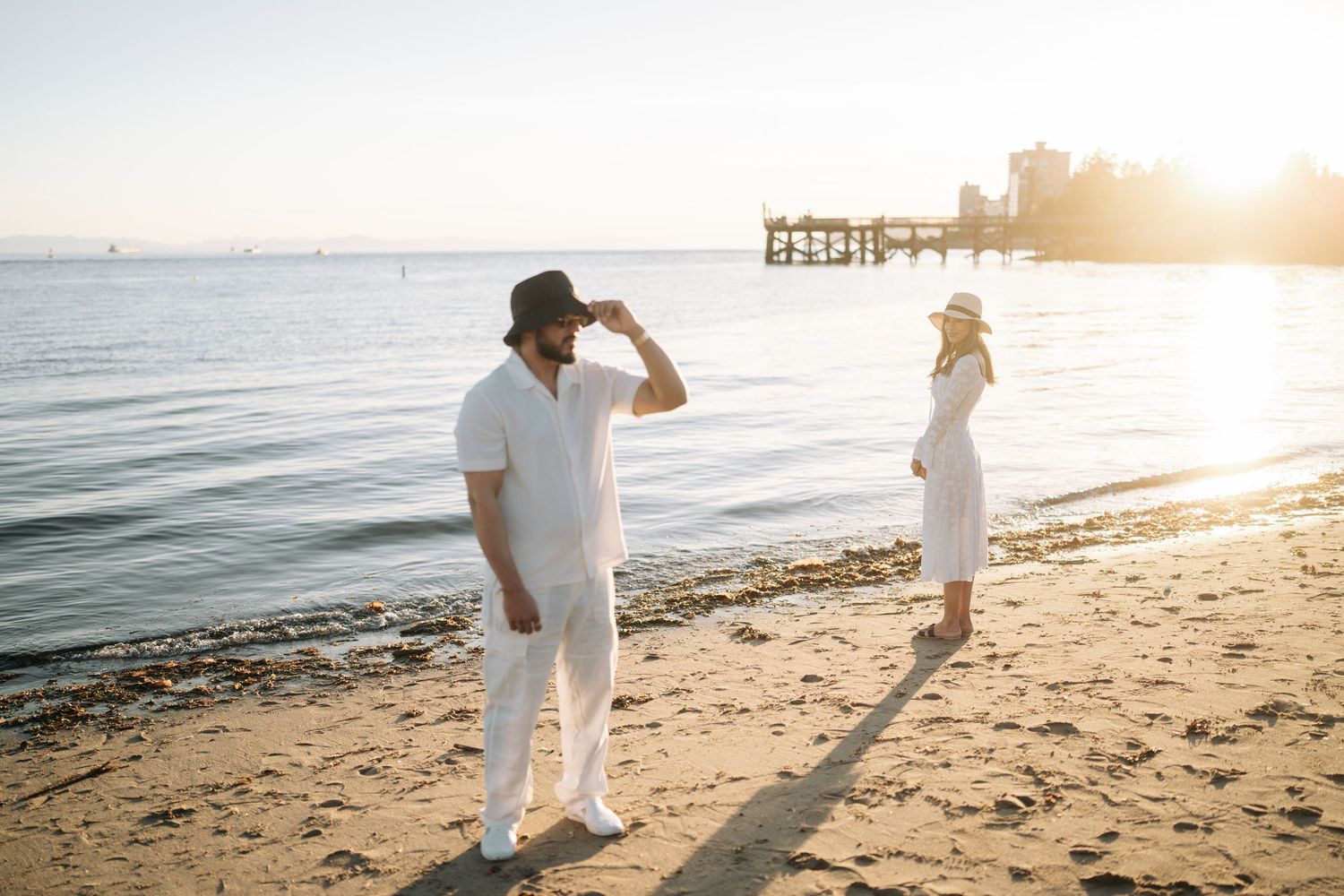 Two people walking on a sandy beach at sunset with golden sunlight creating silhouettes against the ocean.