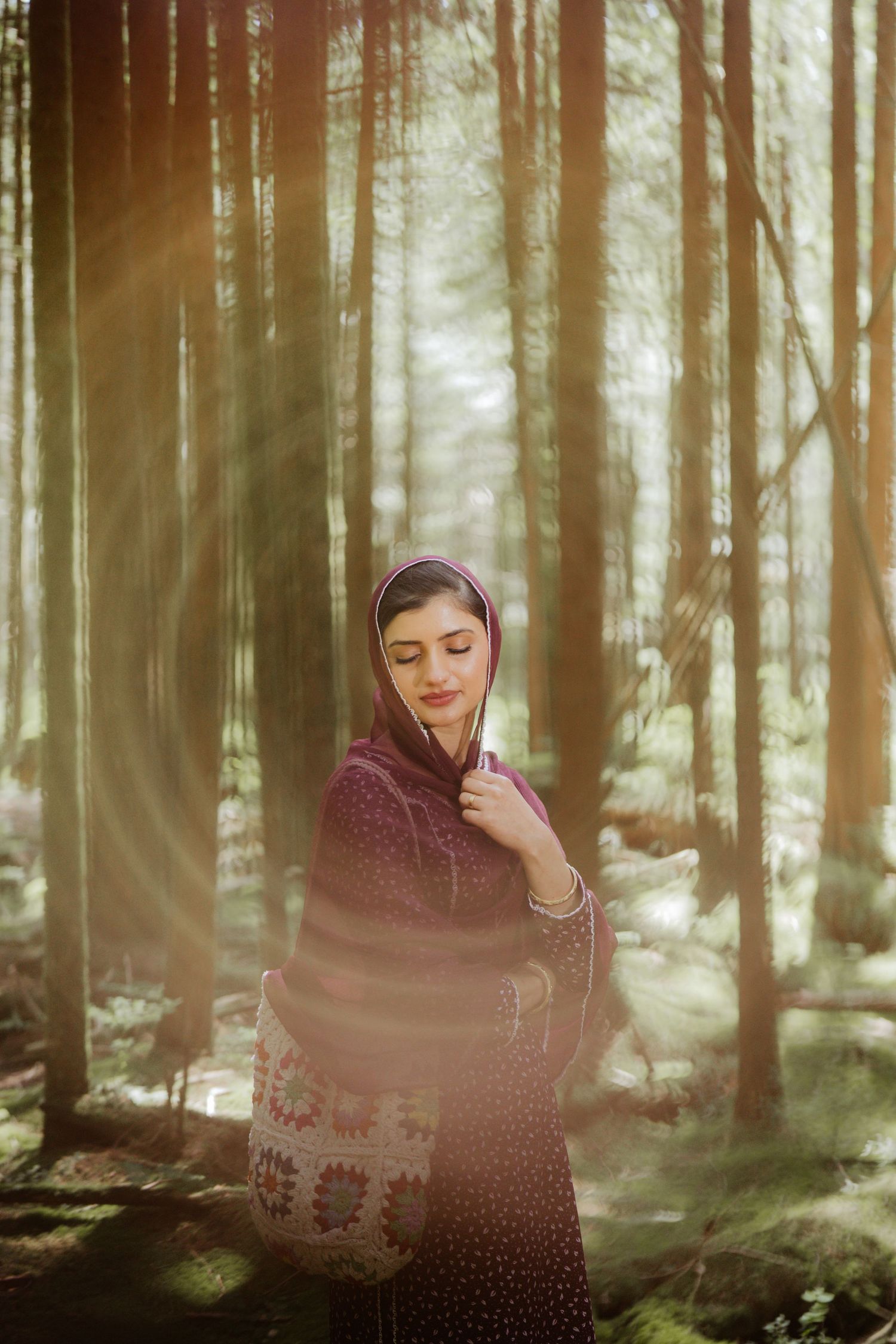 South Asian woman in purple salwar kameez and headscarf bathed in golden sunlight in a serene pine forest.