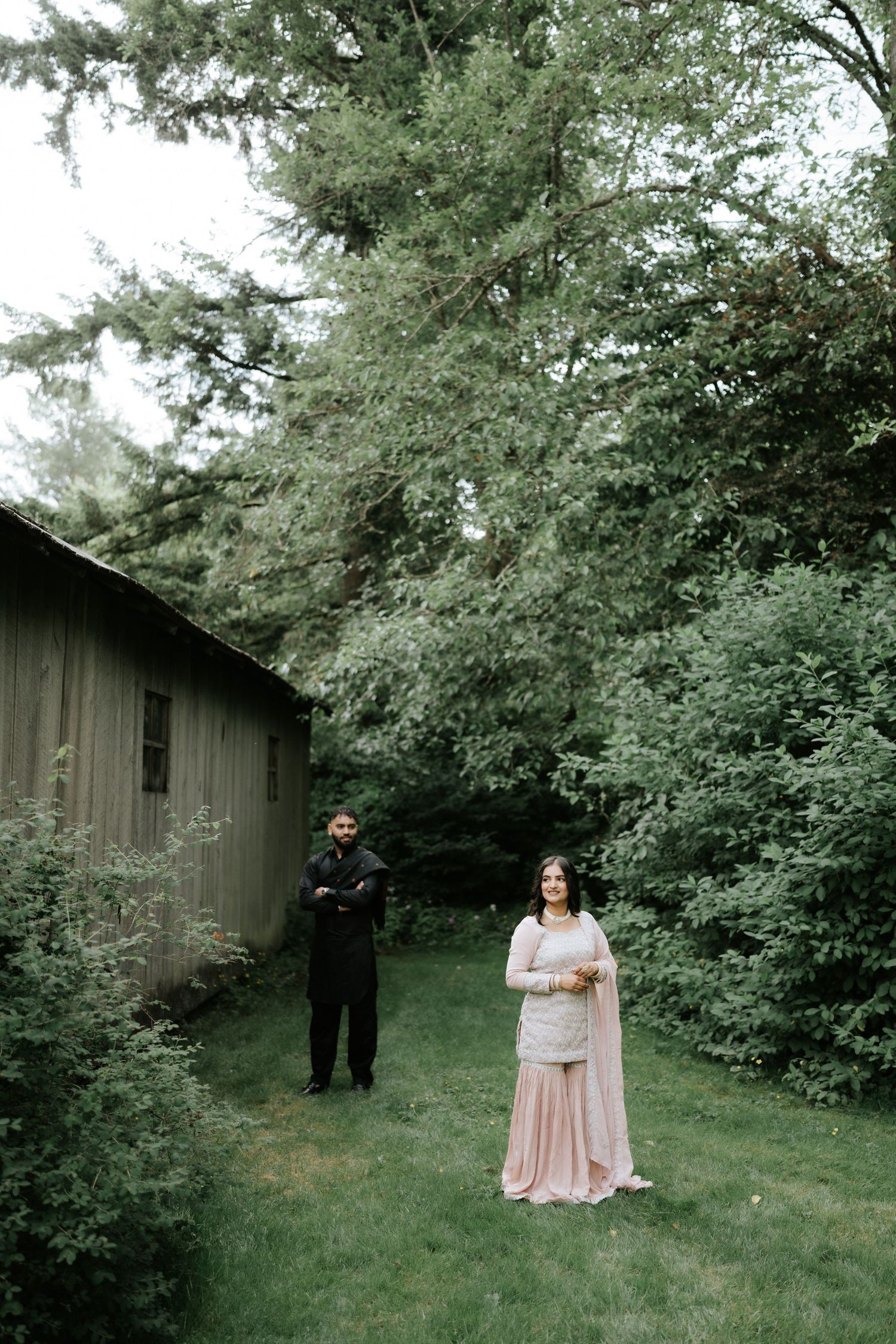 Outdoor portrait session in front of a wooden barn surrounded by green foliage.