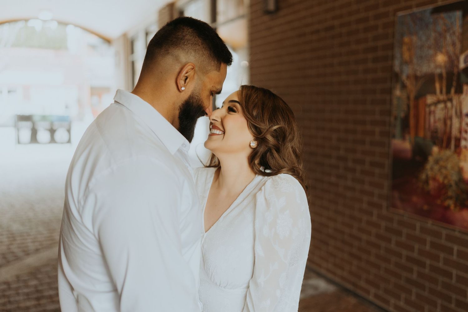 A couple embraces in an architectural setting with brick walls and dramatic lighting.