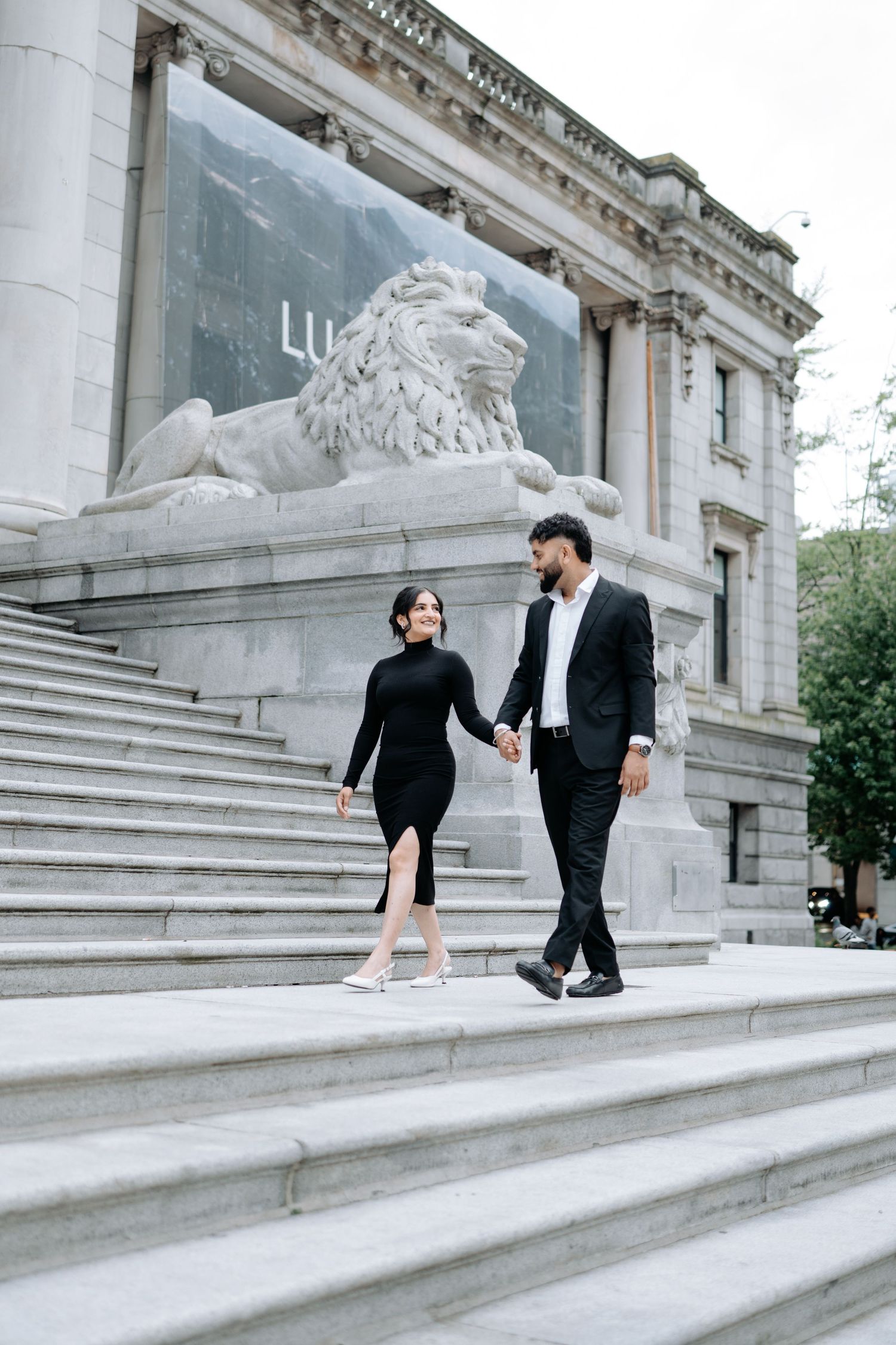 A couple walks together on grand stone steps of a classical building.