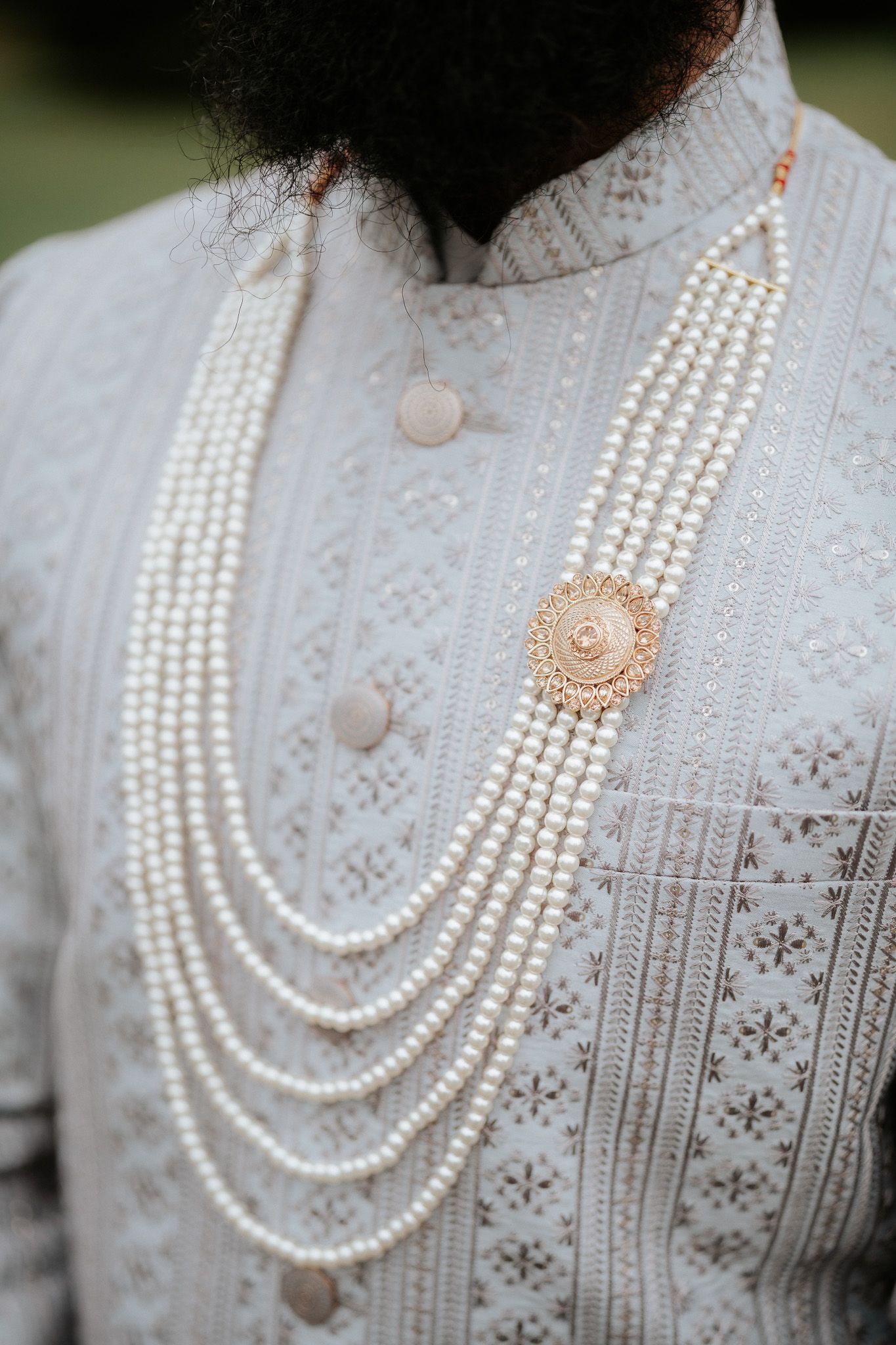 Multi-strand pearl necklace displayed on a white lace dress with intricate floral pattern details.