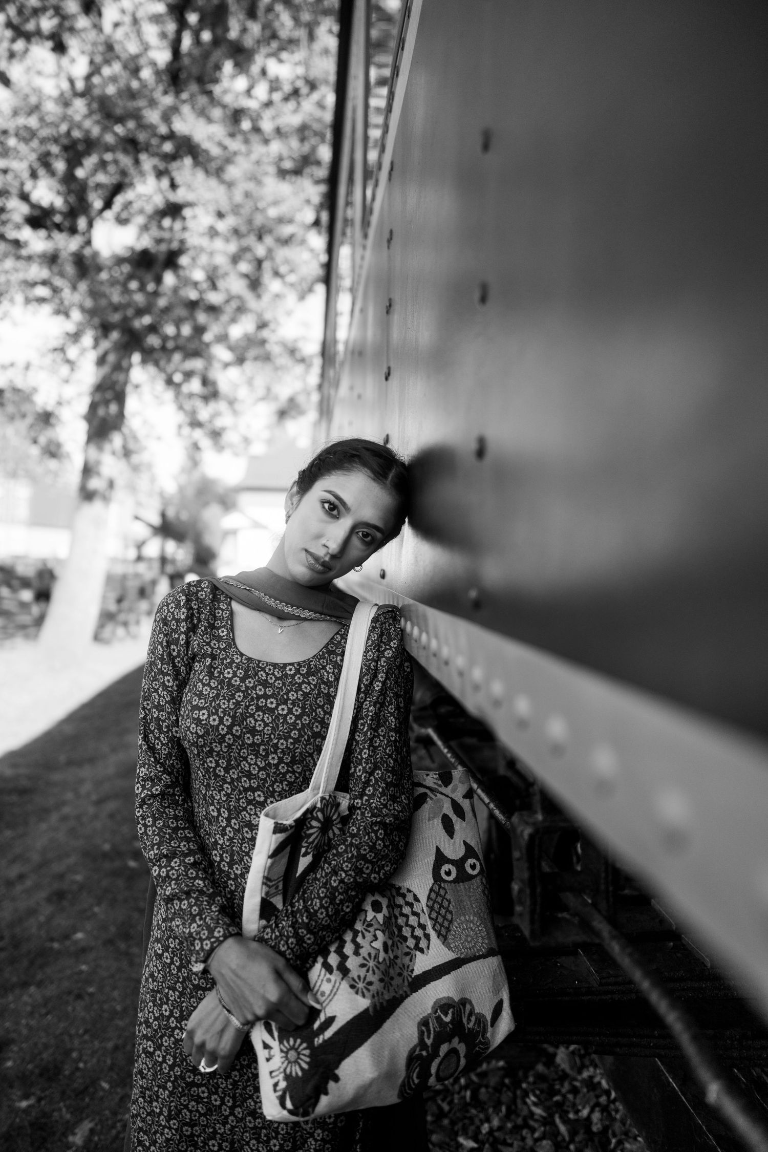 A person in a floral dress poses against a train car in black and white, creating a vintage aesthetic.