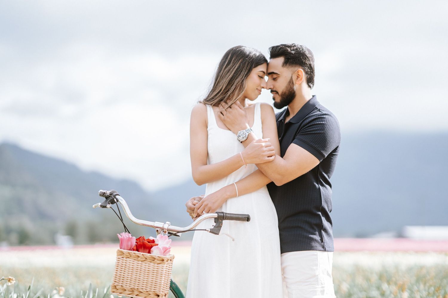 A couple shares a romantic moment in a field with mountains in the background during a picnic date.