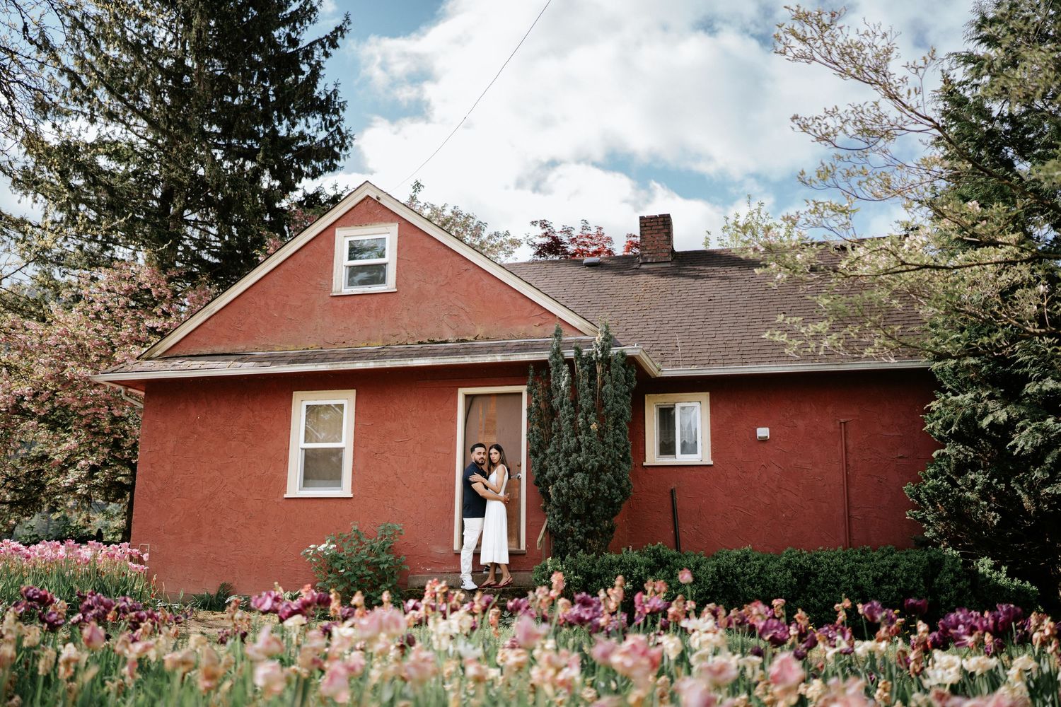 A red brick ranch house with evergreen trees and pink flowers in the garden creates a charming curb appeal.