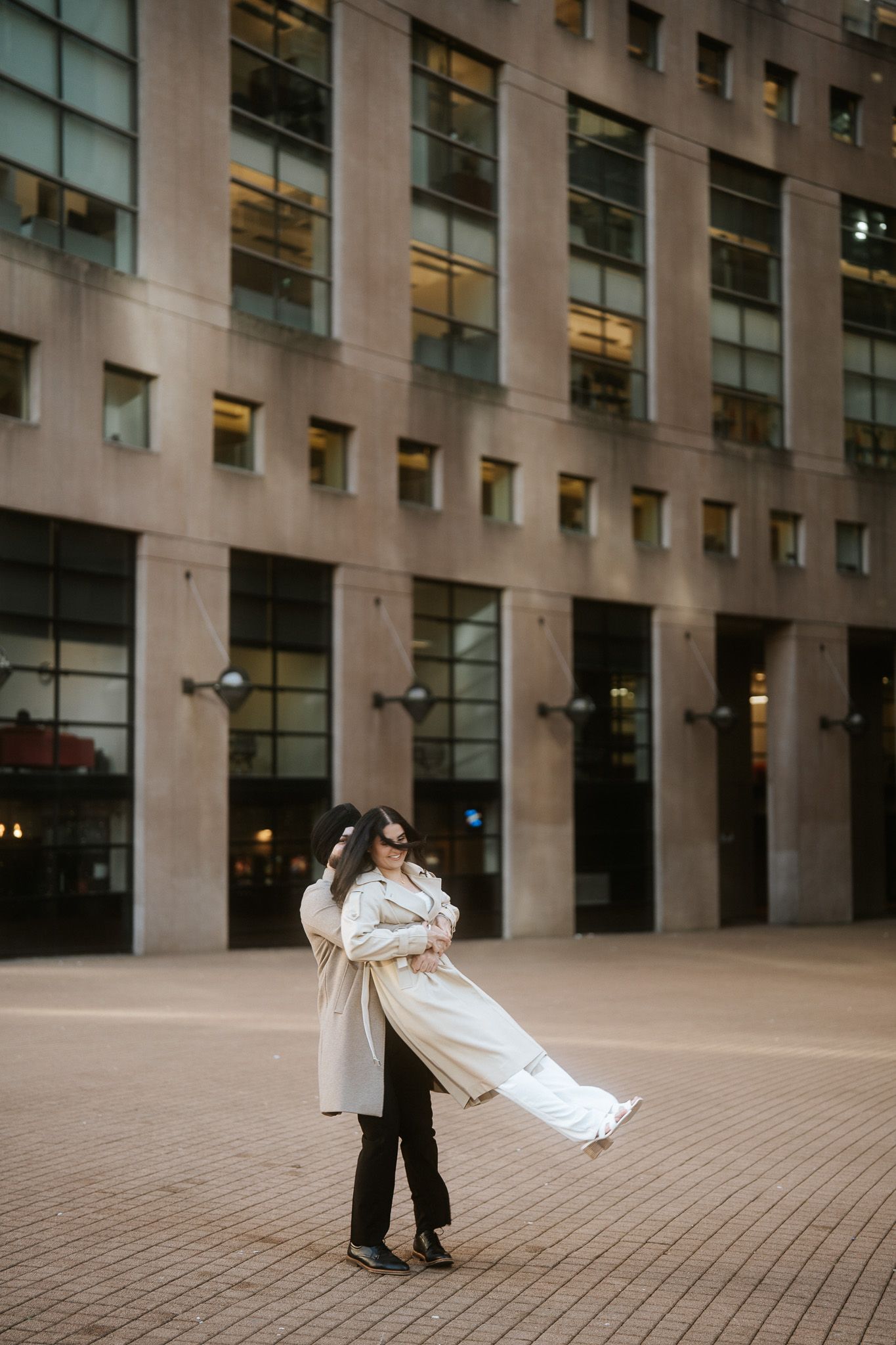 Dancing couple performing elegant moves in an urban plaza surrounded by contemporary office buildings.