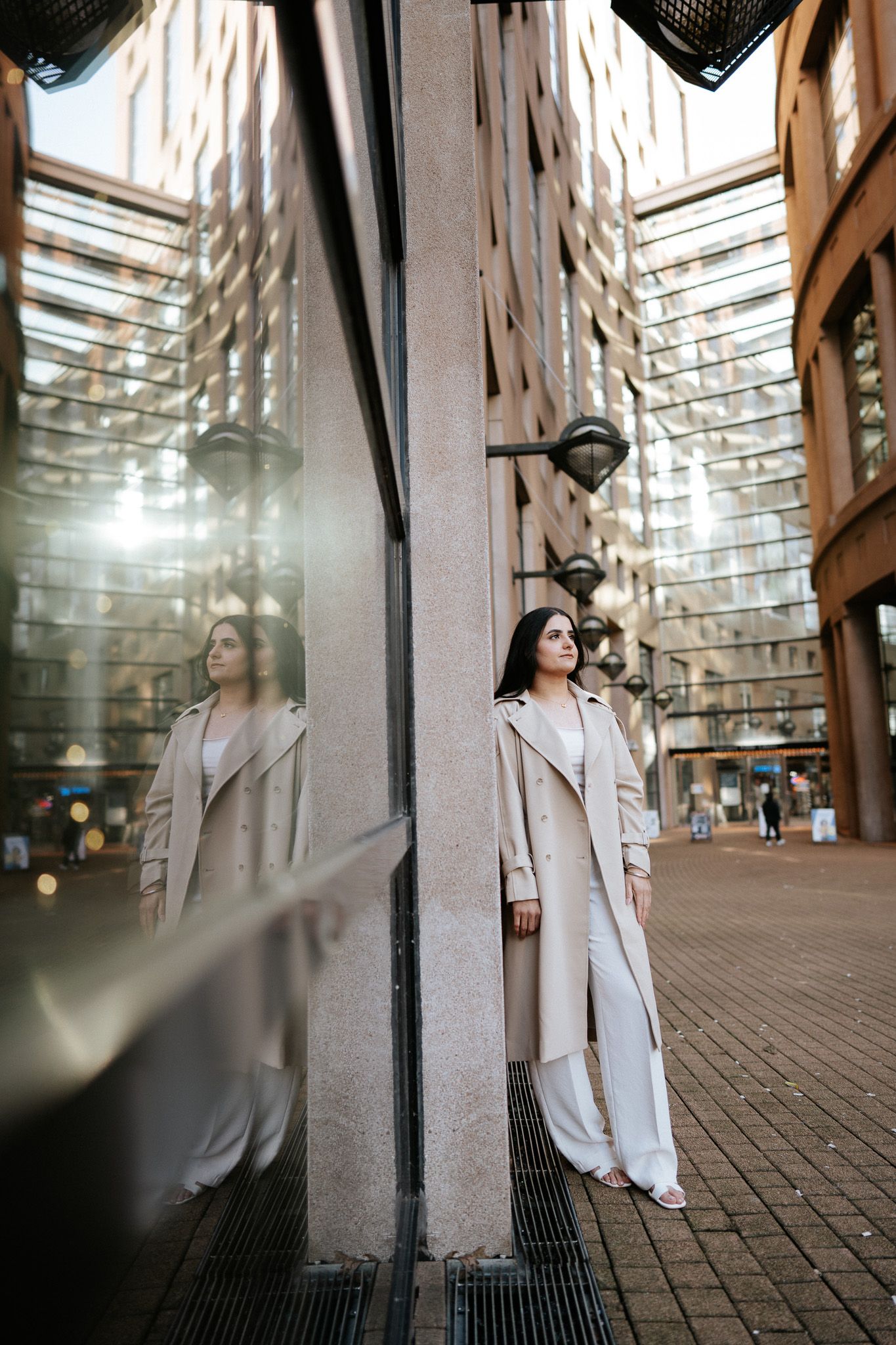 A person in a white dress stands between architectural columns in a curved brick walkway with dramatic lighting.