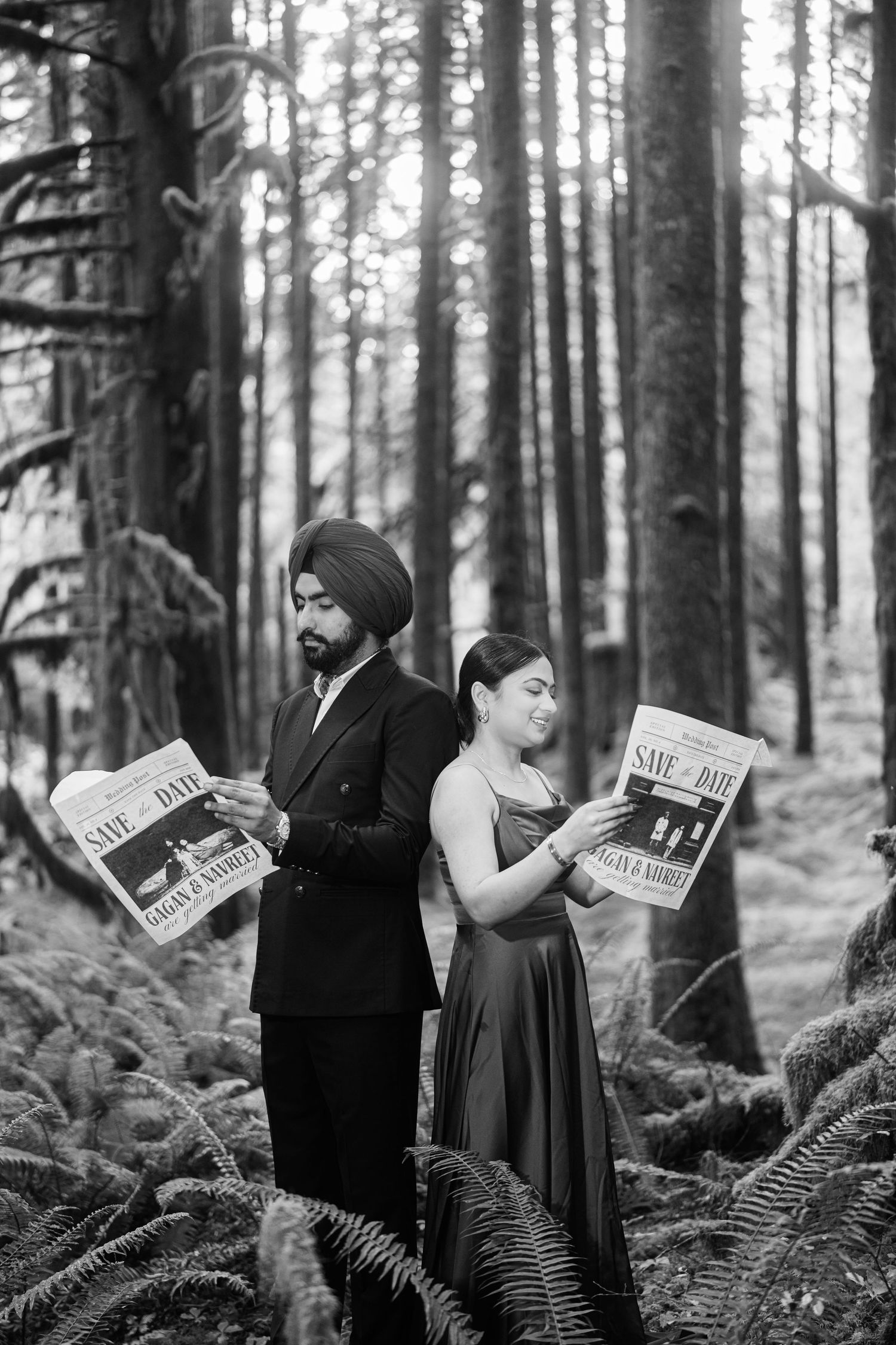 Black and white photo of two people reading newspapers while standing in a forest with ferns.