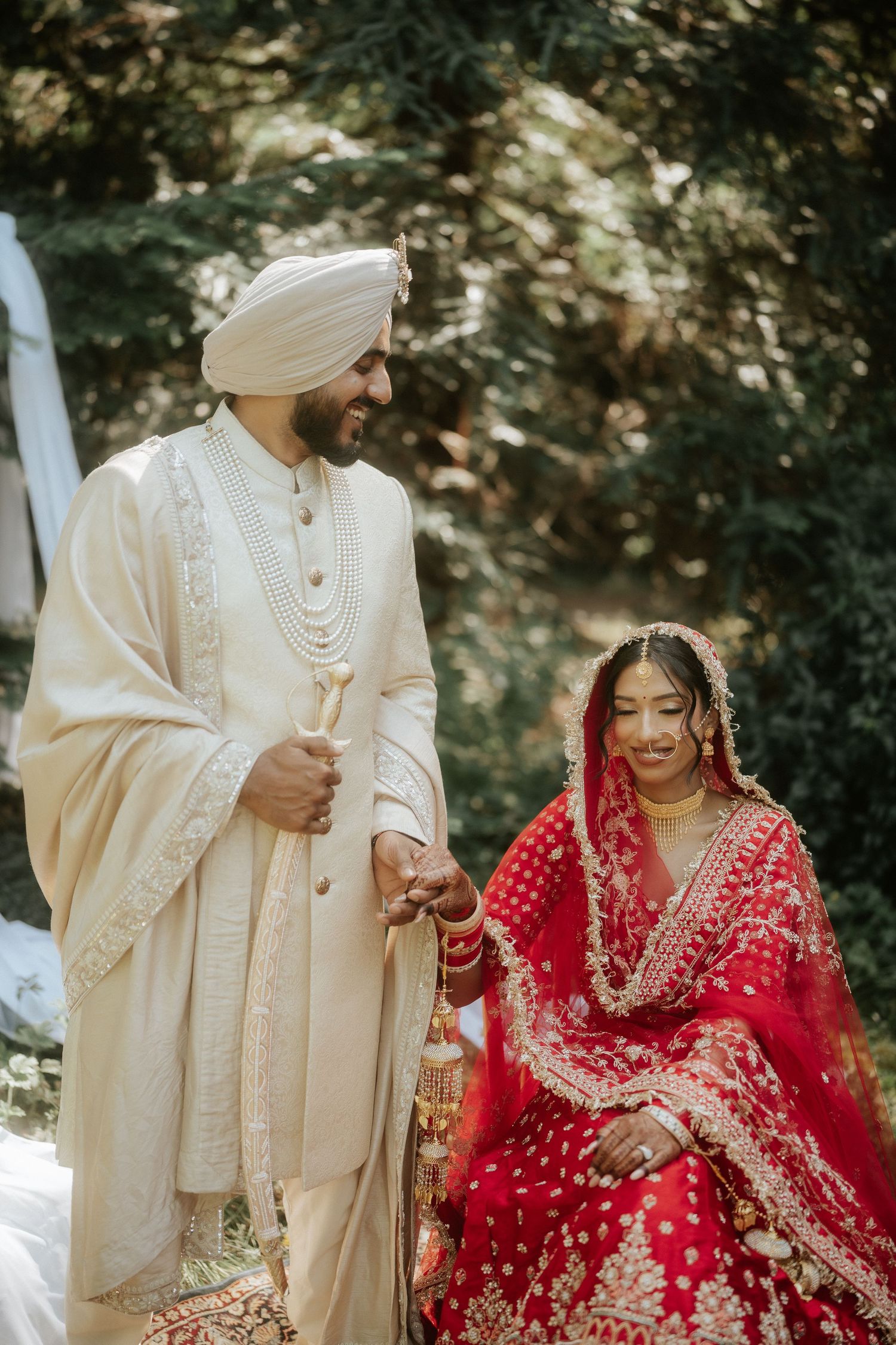A wedding couple in traditional Sikh attire poses together in an outdoor setting.