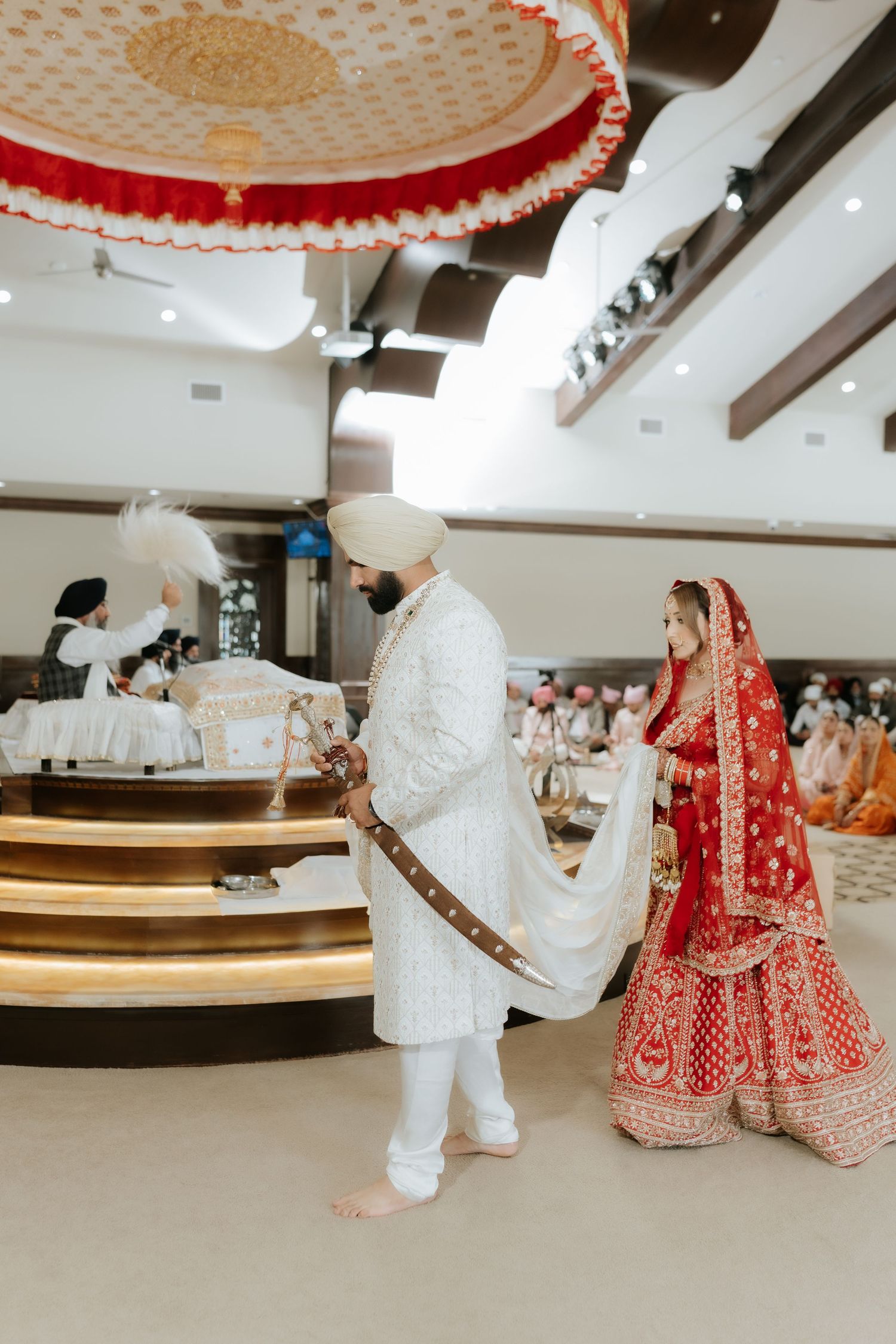 Sikh wedding couple in traditional attire performing Anand Karaj ceremony inside a Gurdwara.