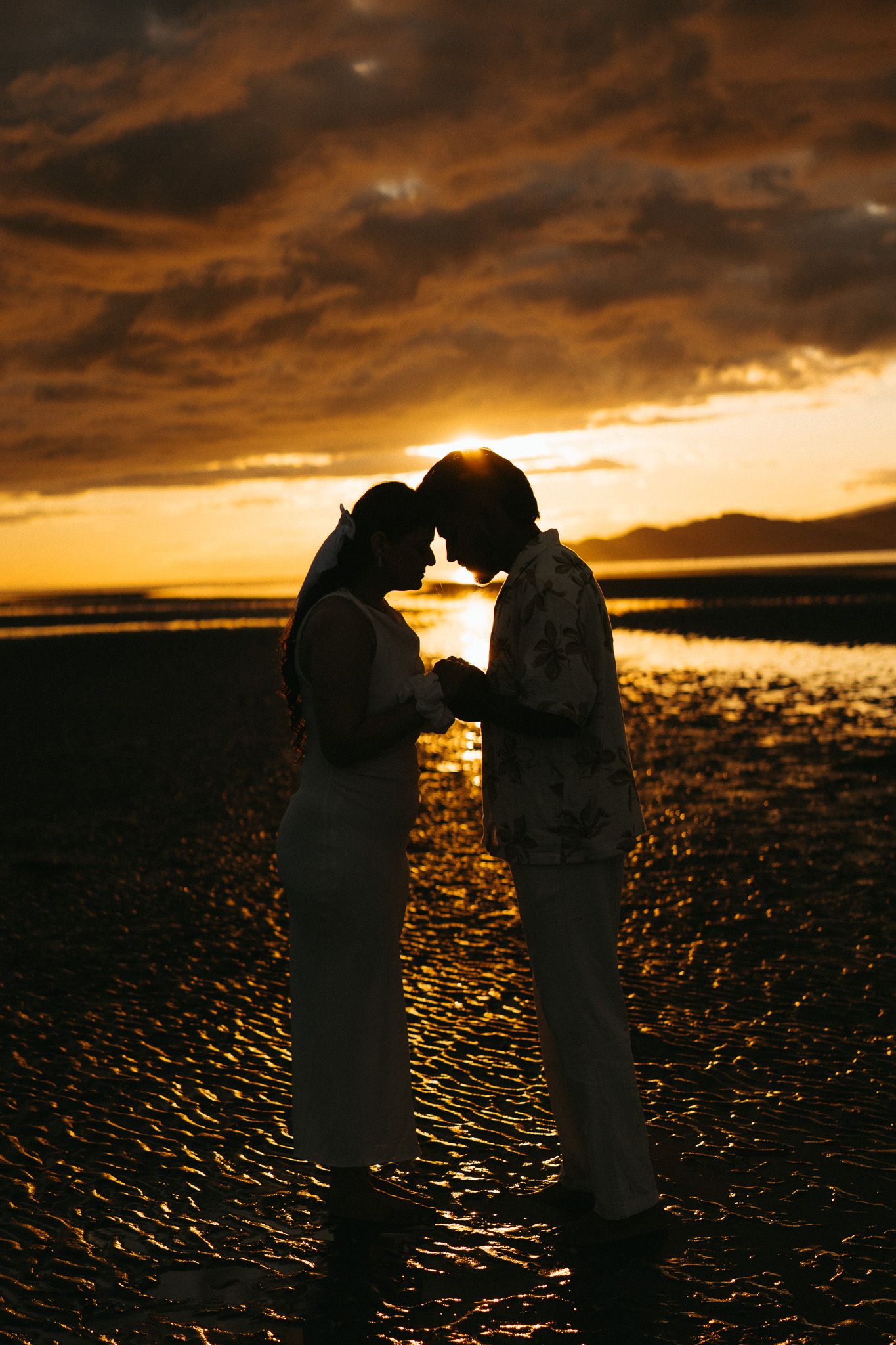 A romantic silhouette of a couple touching foreheads against a dramatic golden sunset over a beach.