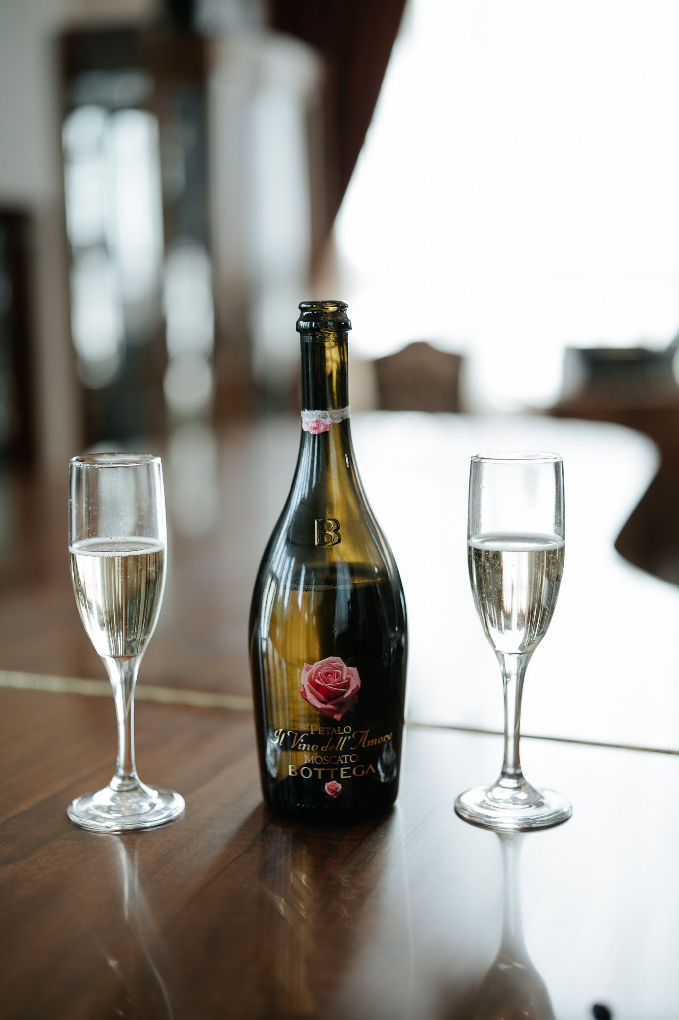 Elegant bottle of Bottega sparkling wine flanked by two champagne flutes on a wooden table.