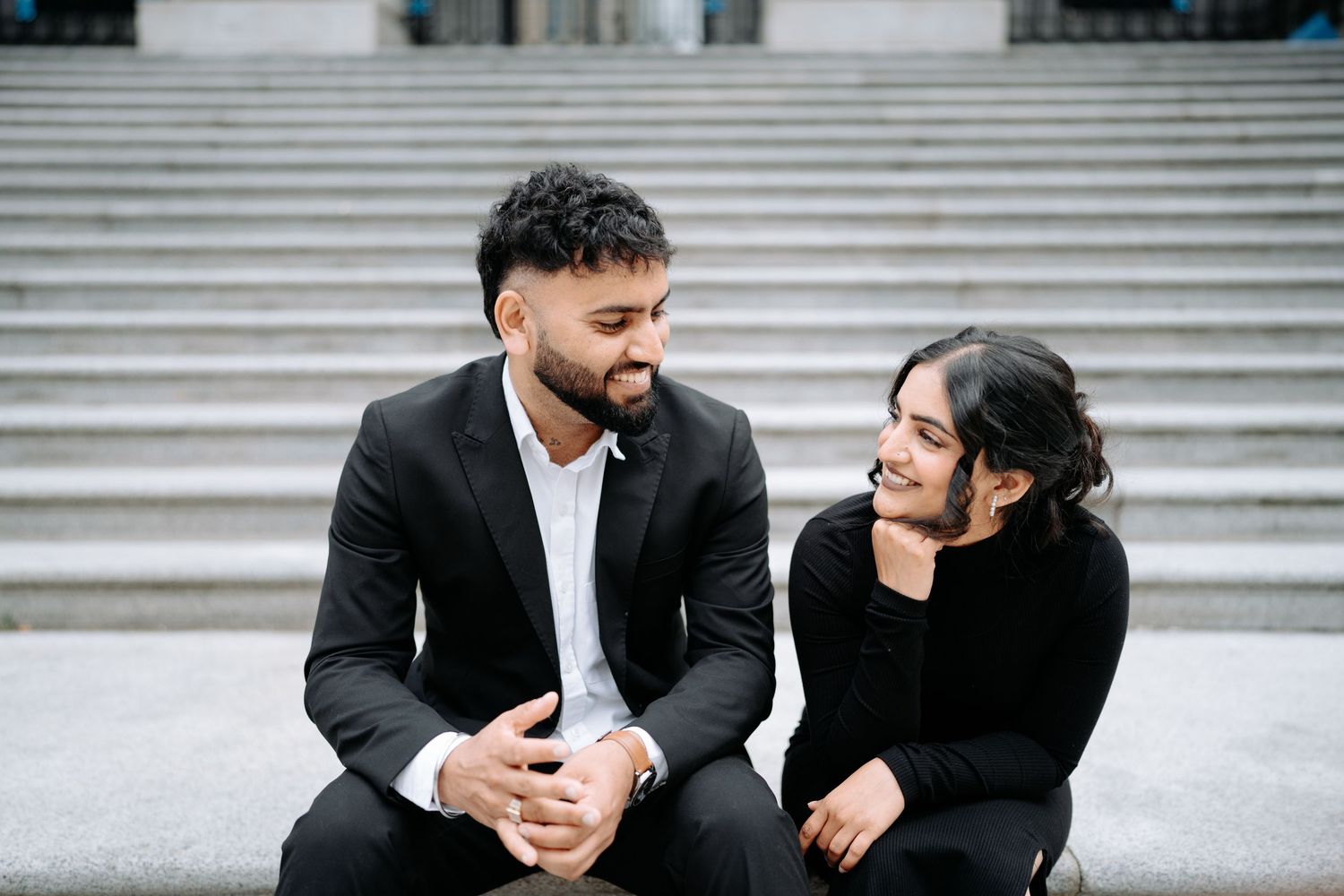 A couple shares playful moments while sitting on marble steps of a historic building.