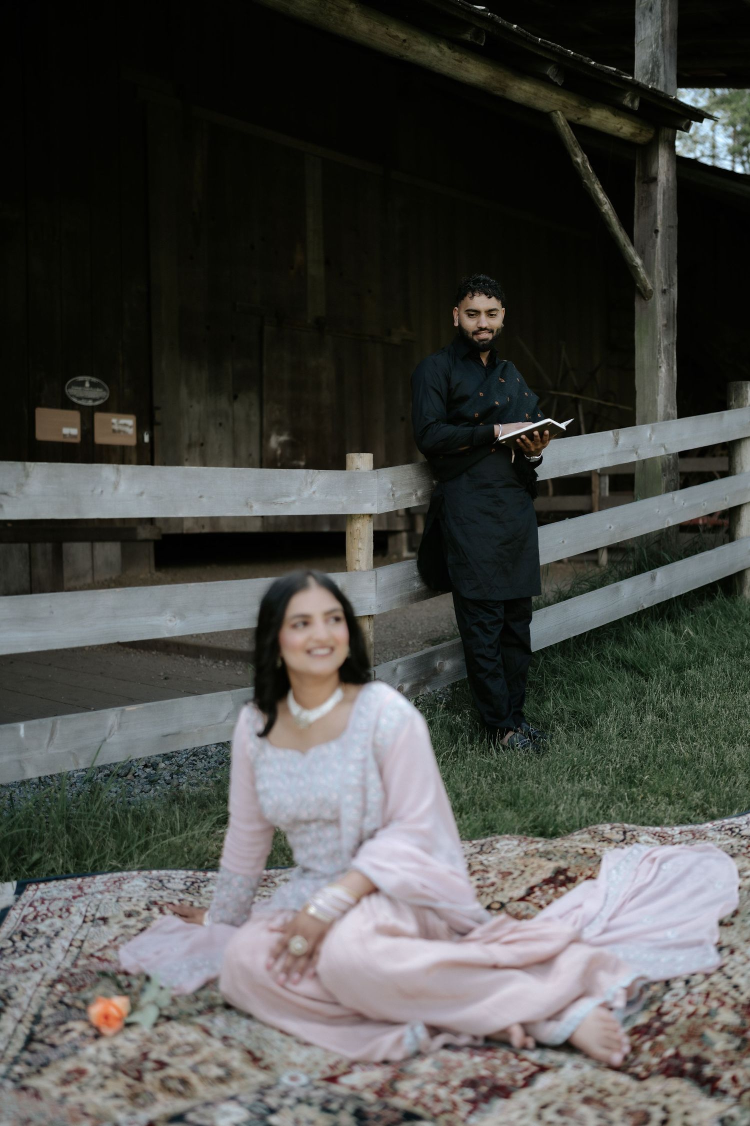 A couple in contrasting outfits poses near a rustic wooden barn with a picnic setup.