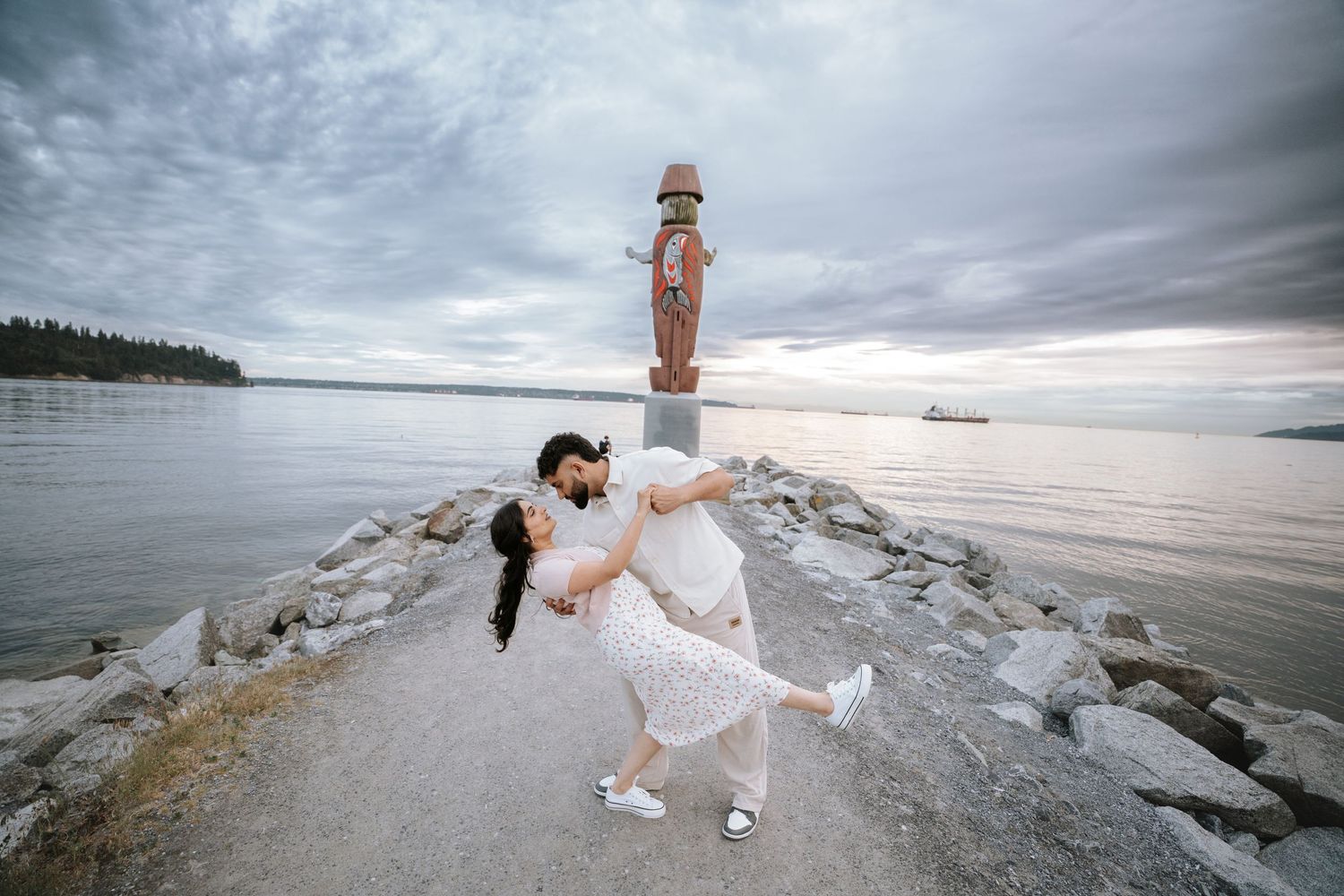 A couple shares a romantic moment on a rocky coastal outcrop during sunset.