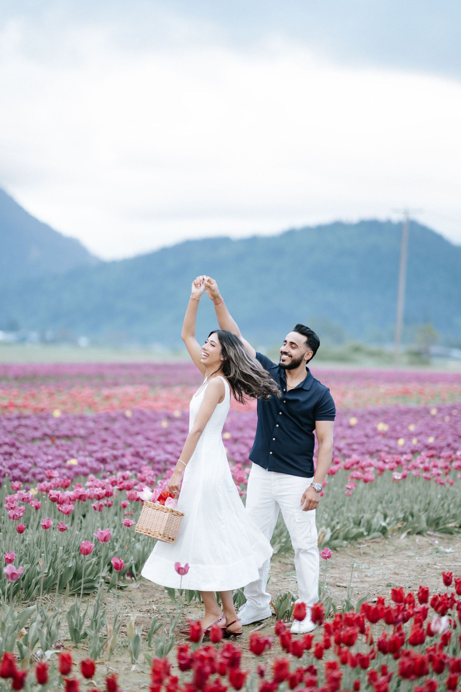 A couple dances joyfully together in a vibrant field of red tulips with mountains in the background.