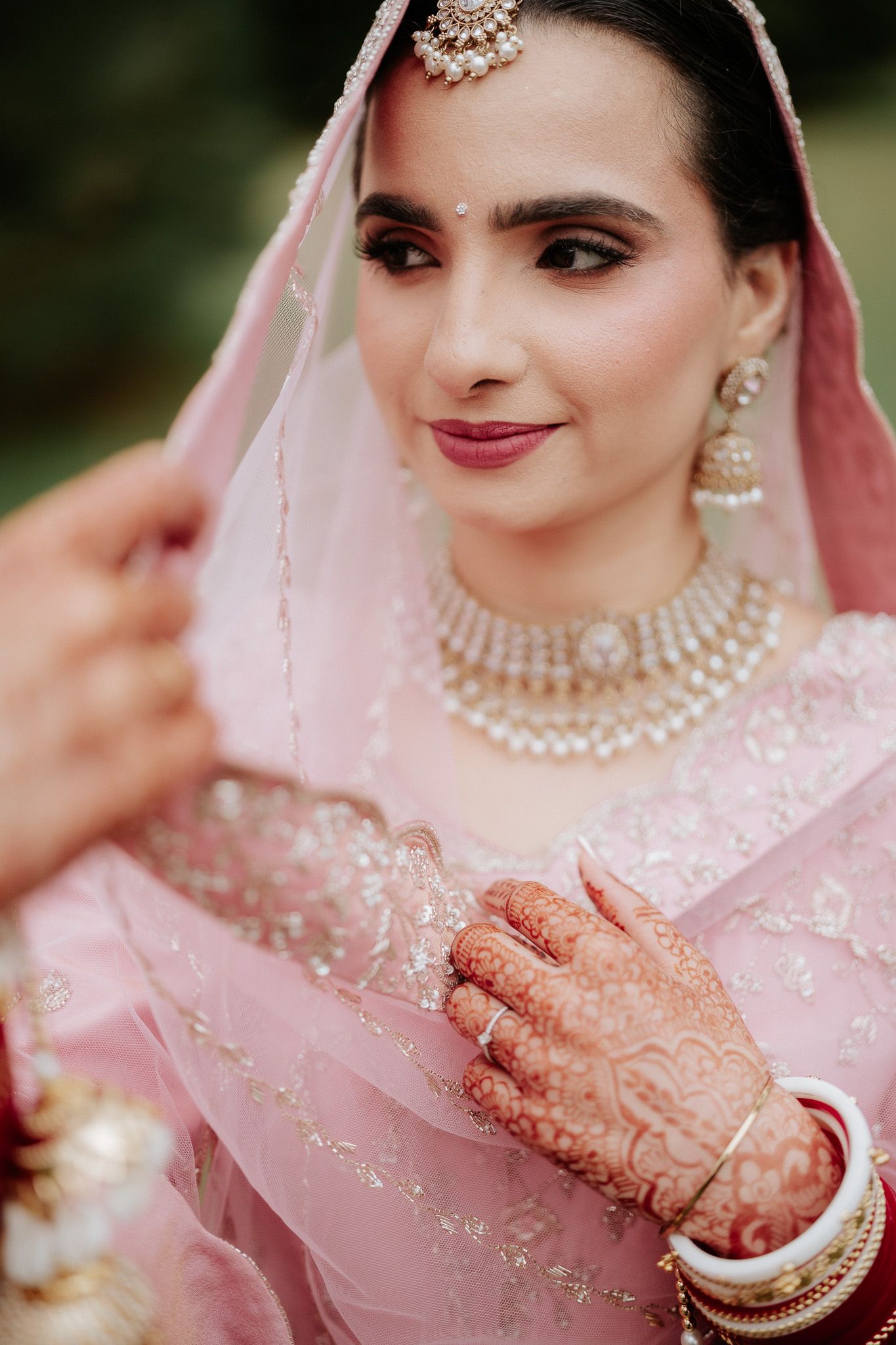 Close-up details of traditional Indian bridal jewelry and pink attire with intricate henna designs and embellishments.