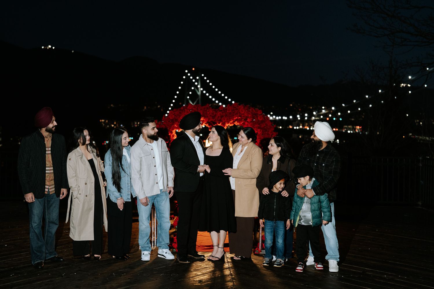 A group of people standing together at night with the illuminated Brooklyn Bridge lights visible in the background.