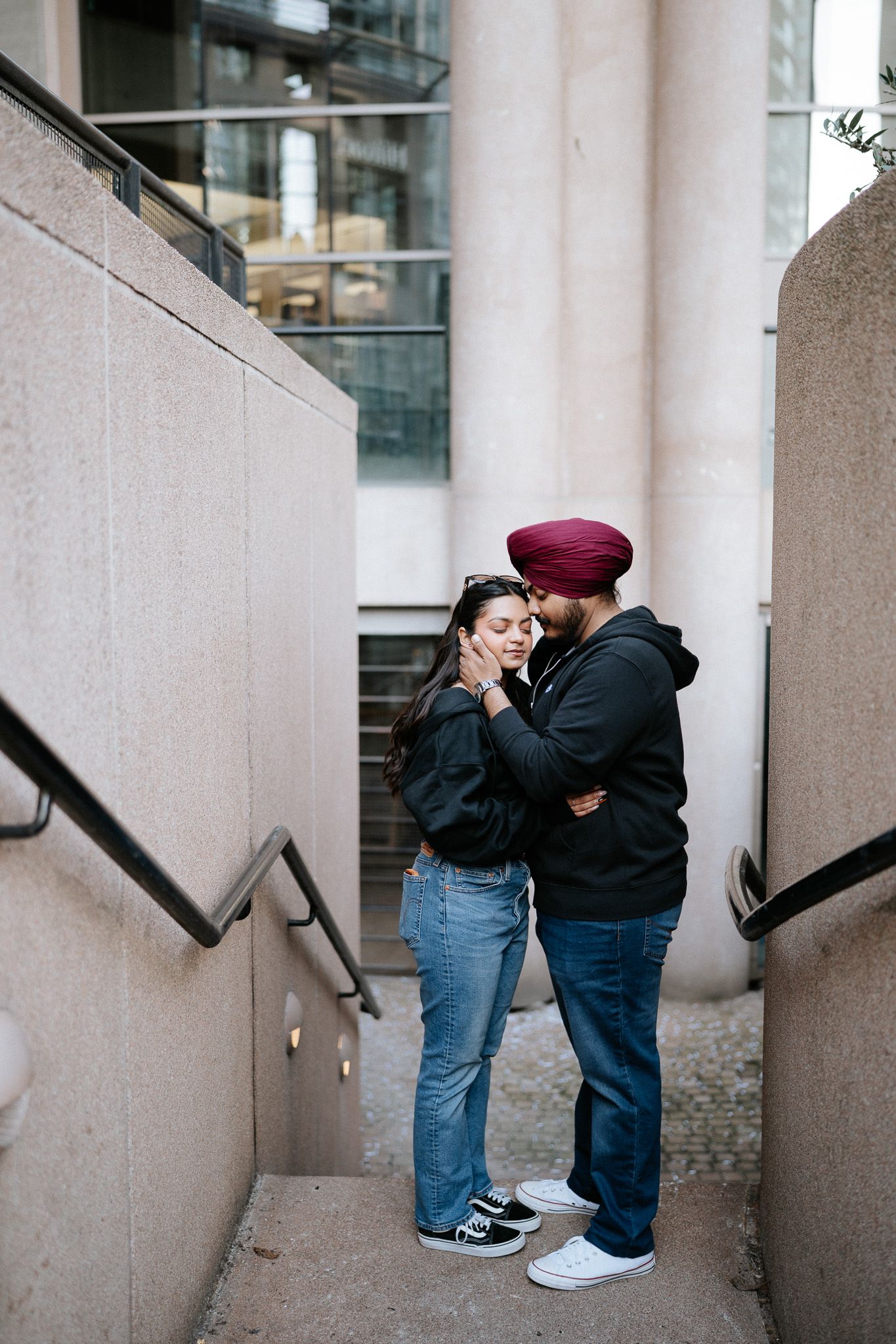 A couple embraces on concrete steps between walls, wearing casual clothing and sharing an intimate moment.