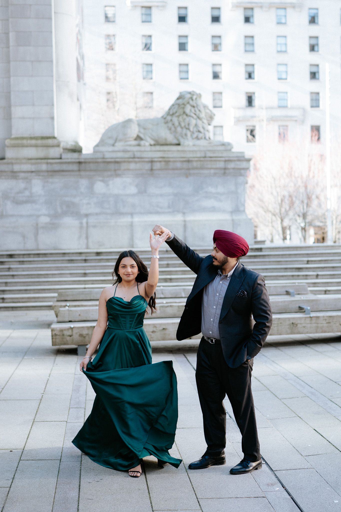 A couple in formal attire dances playfully on stone steps, with the woman twirling in an emerald green gown.