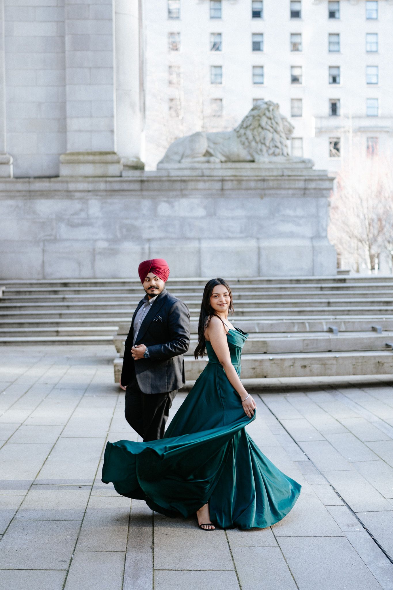 A couple in formal attire poses elegantly on stone steps, with the woman wearing a flowing emerald green gown.