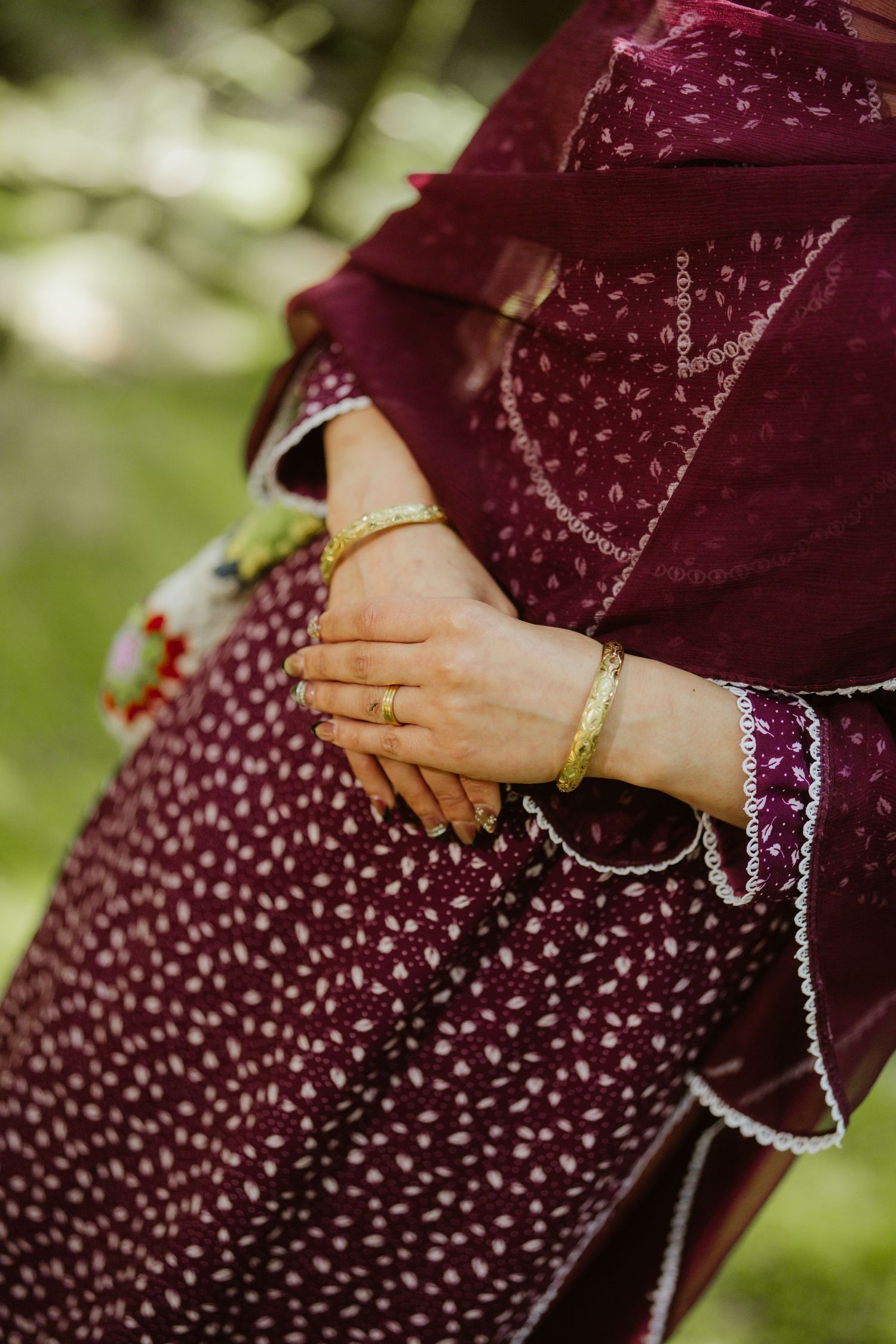 Close-up of South Asian woman's hands adorned with gold bangles and rings in a burgundy embroidered salwar kameez.