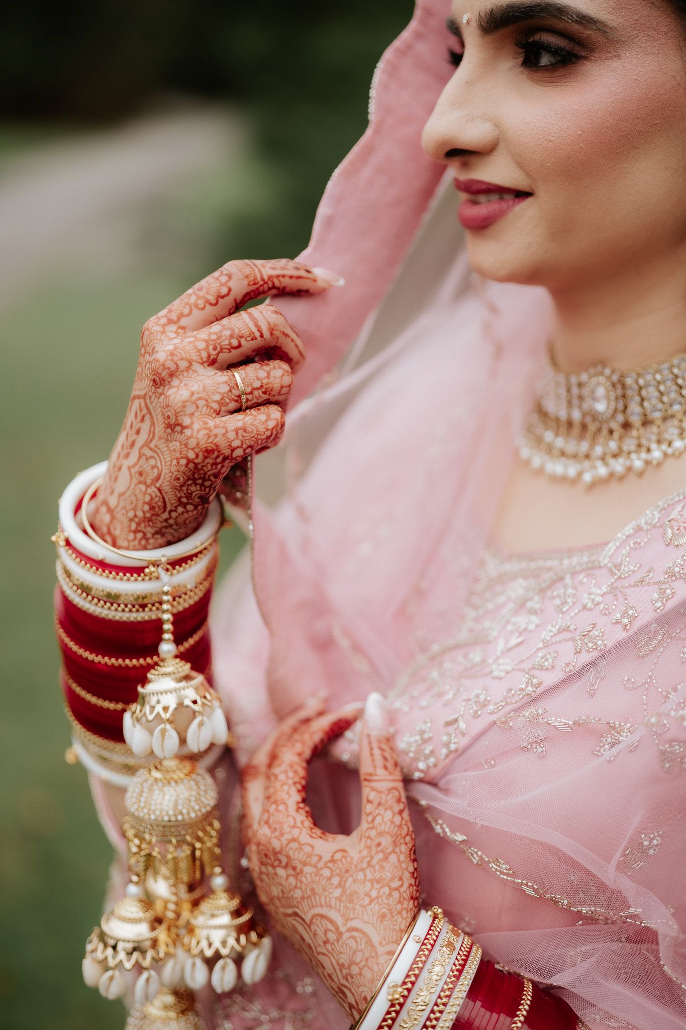 Traditional Indian bridal jewelry and henna adorned hands with delicate pink embroidered attire.