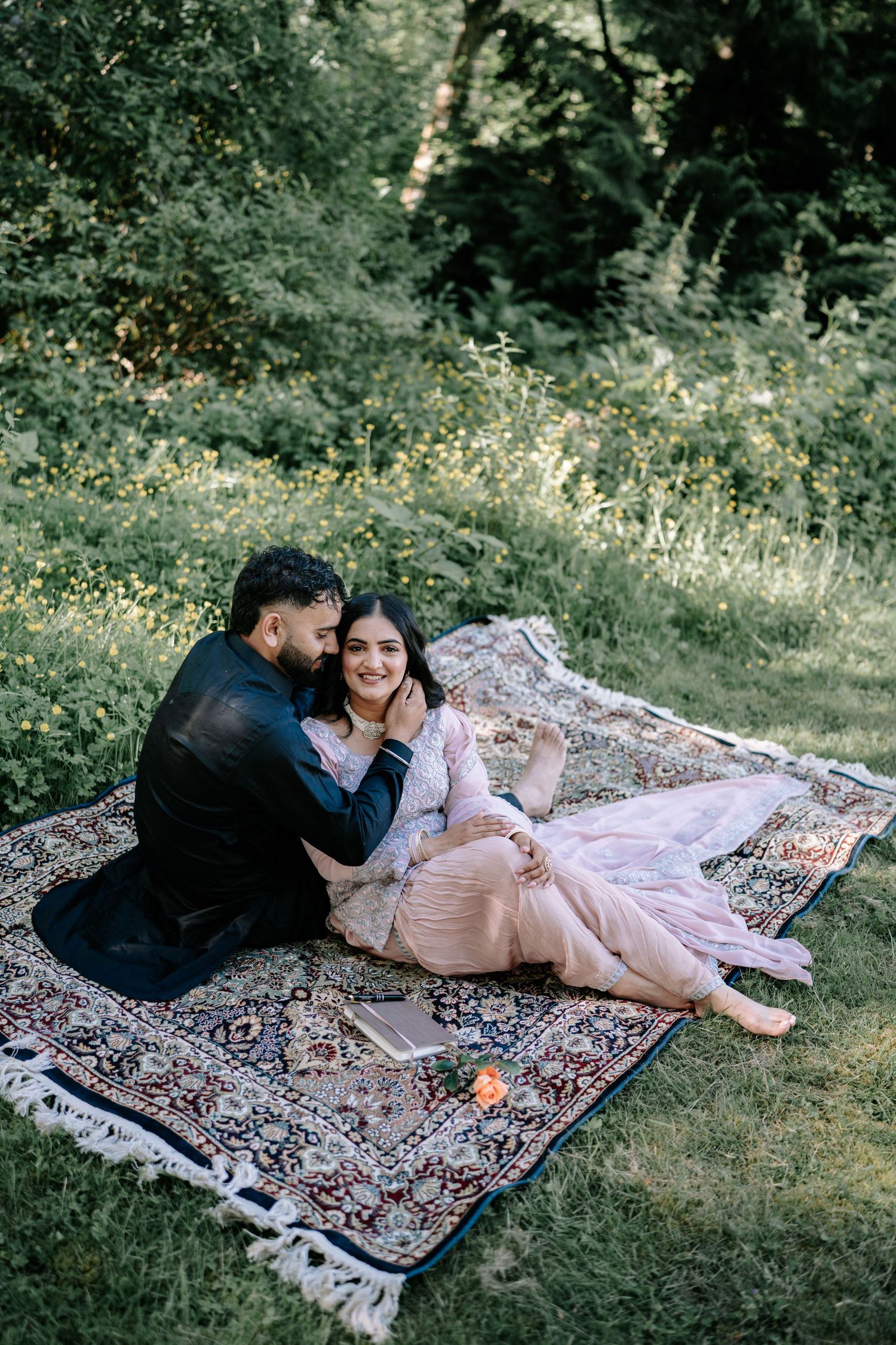A couple relaxes on a patterned blanket in a grassy outdoor setting.