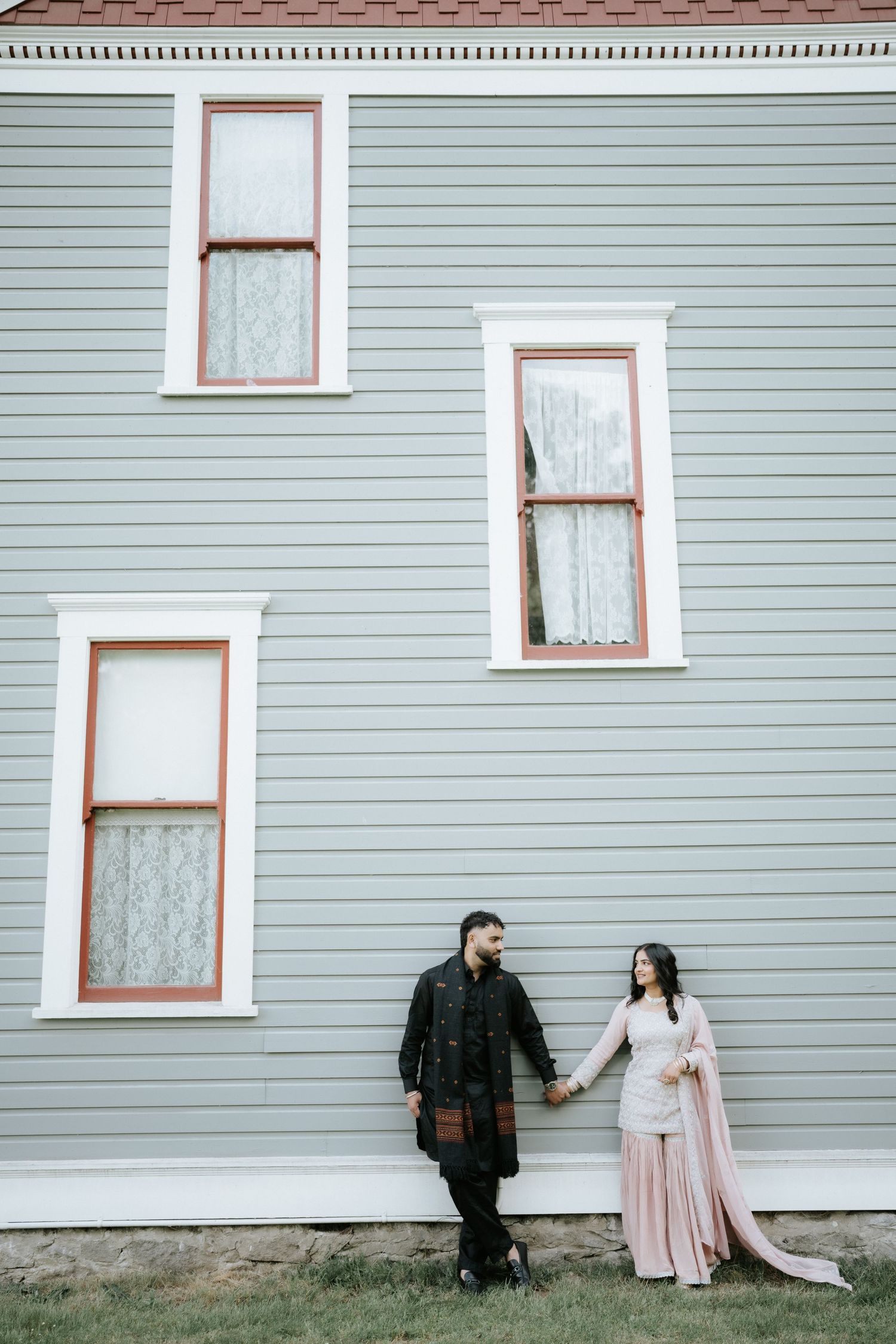A couple takes artistic portraits against a large gray house with white-trimmed windows.
