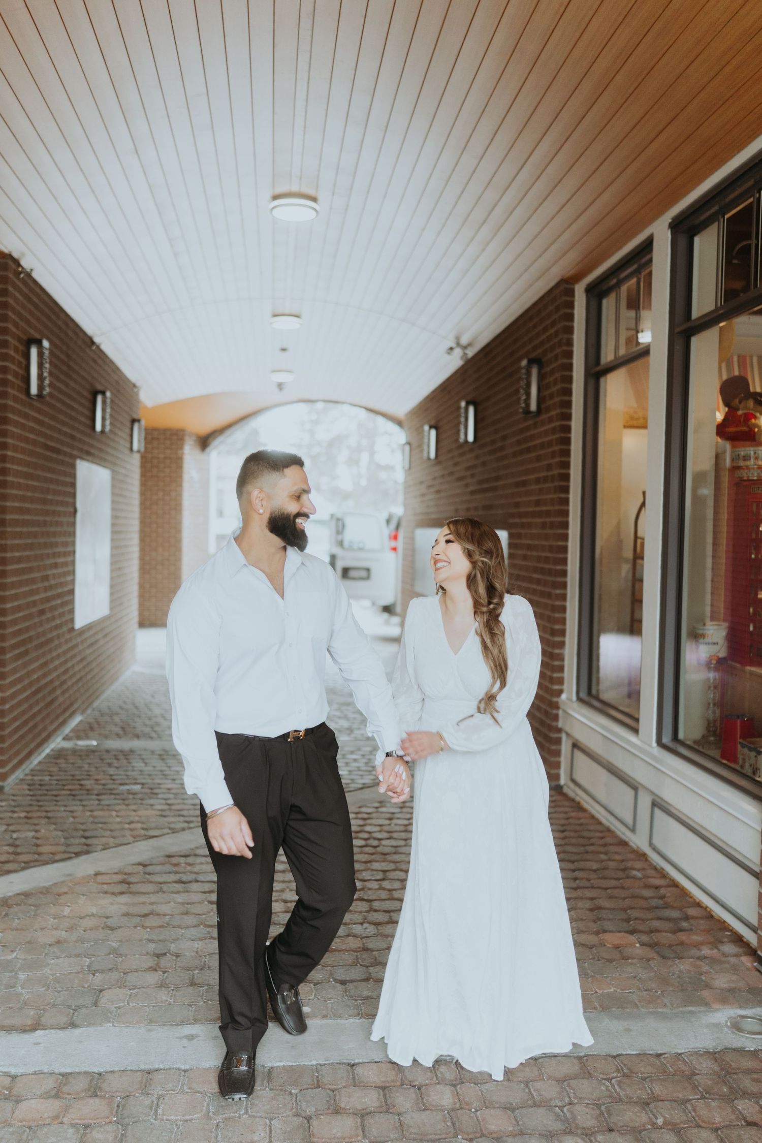 A couple walks together along a brick-lined corridor with white ceiling panels.