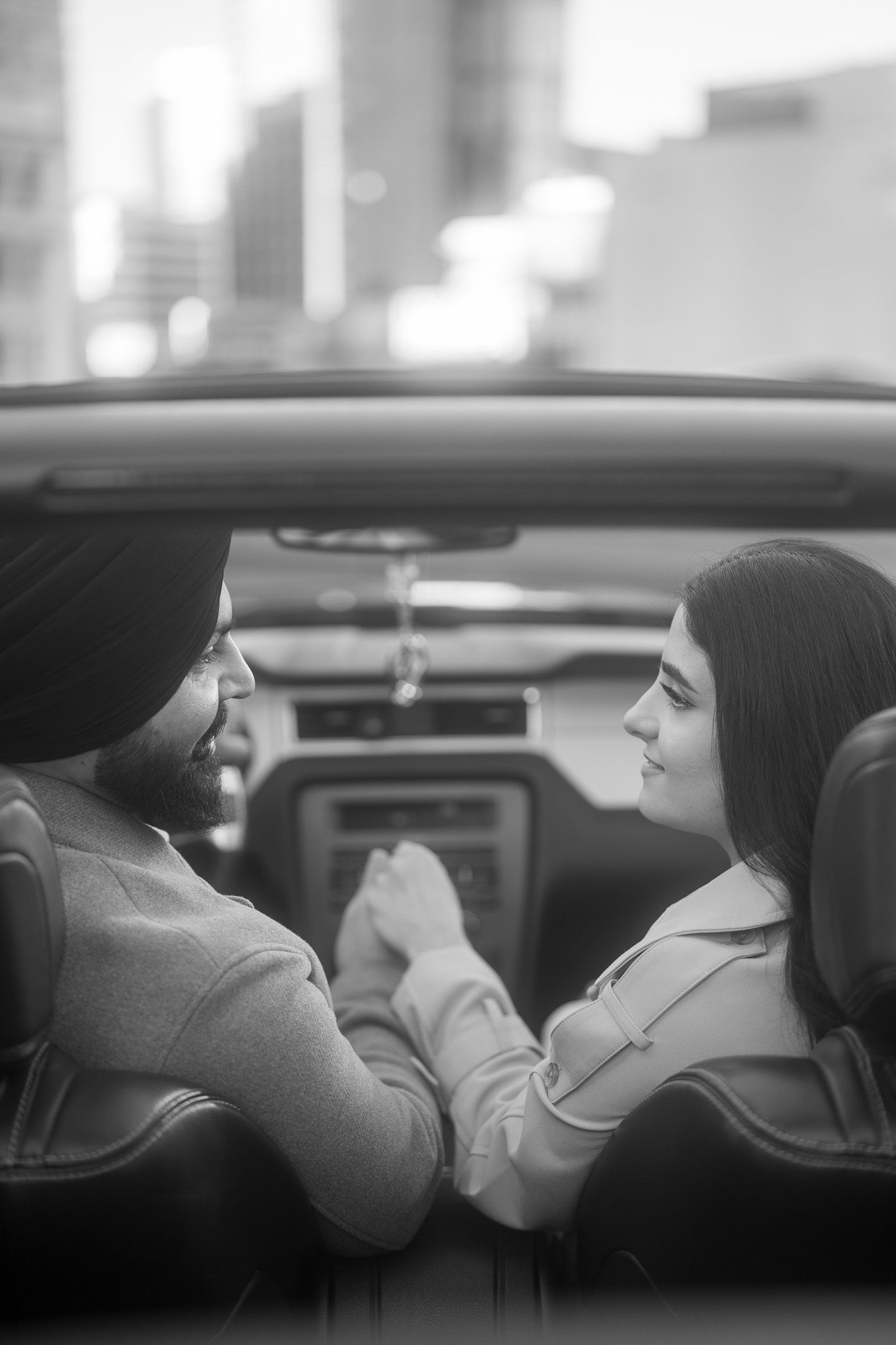 Black and white photo of a couple sitting together in a car, holding hands and gazing at each other.