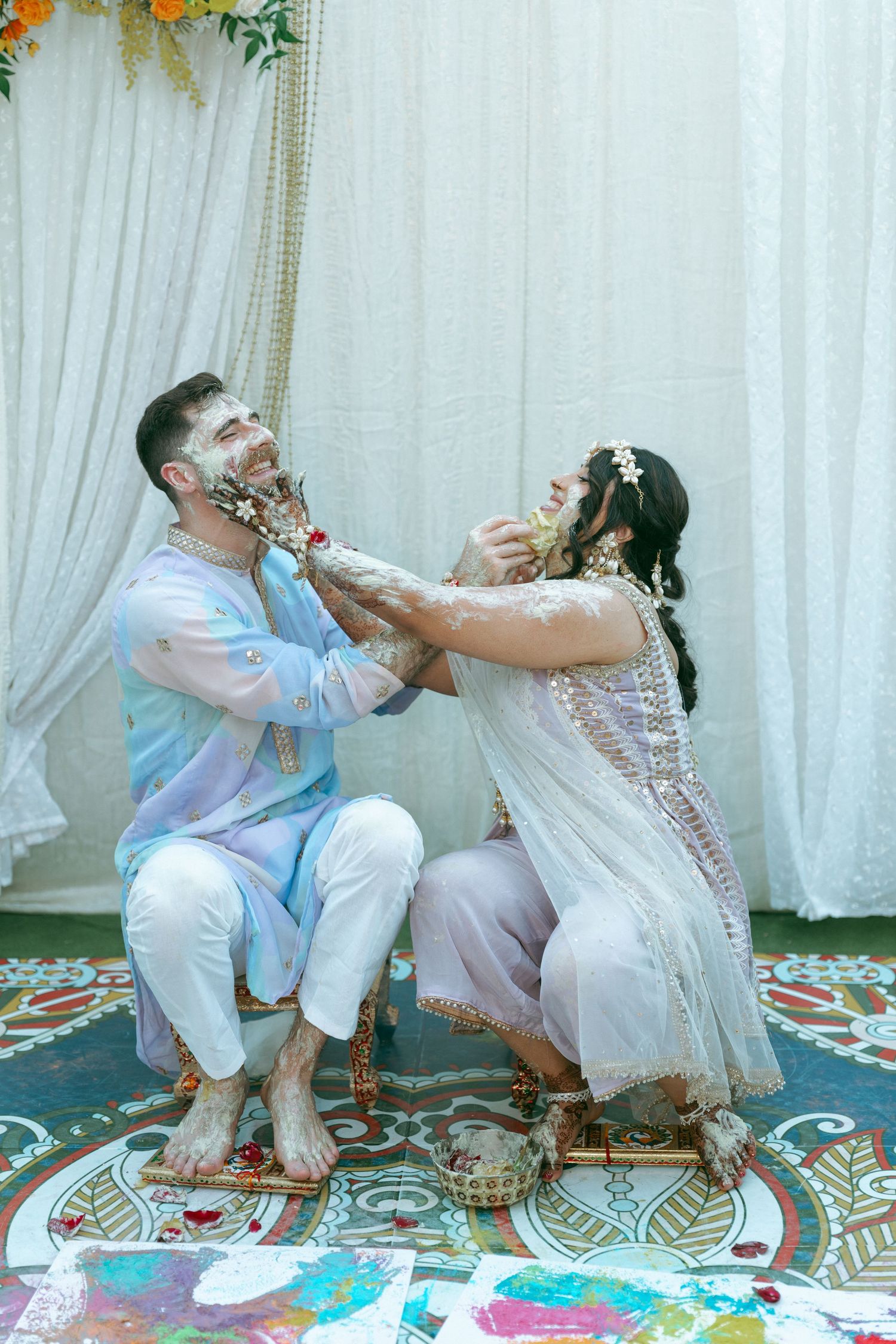 Couple playfully applying haldi paste during traditional Indian wedding ceremony, dressed in light blue and white outfits.