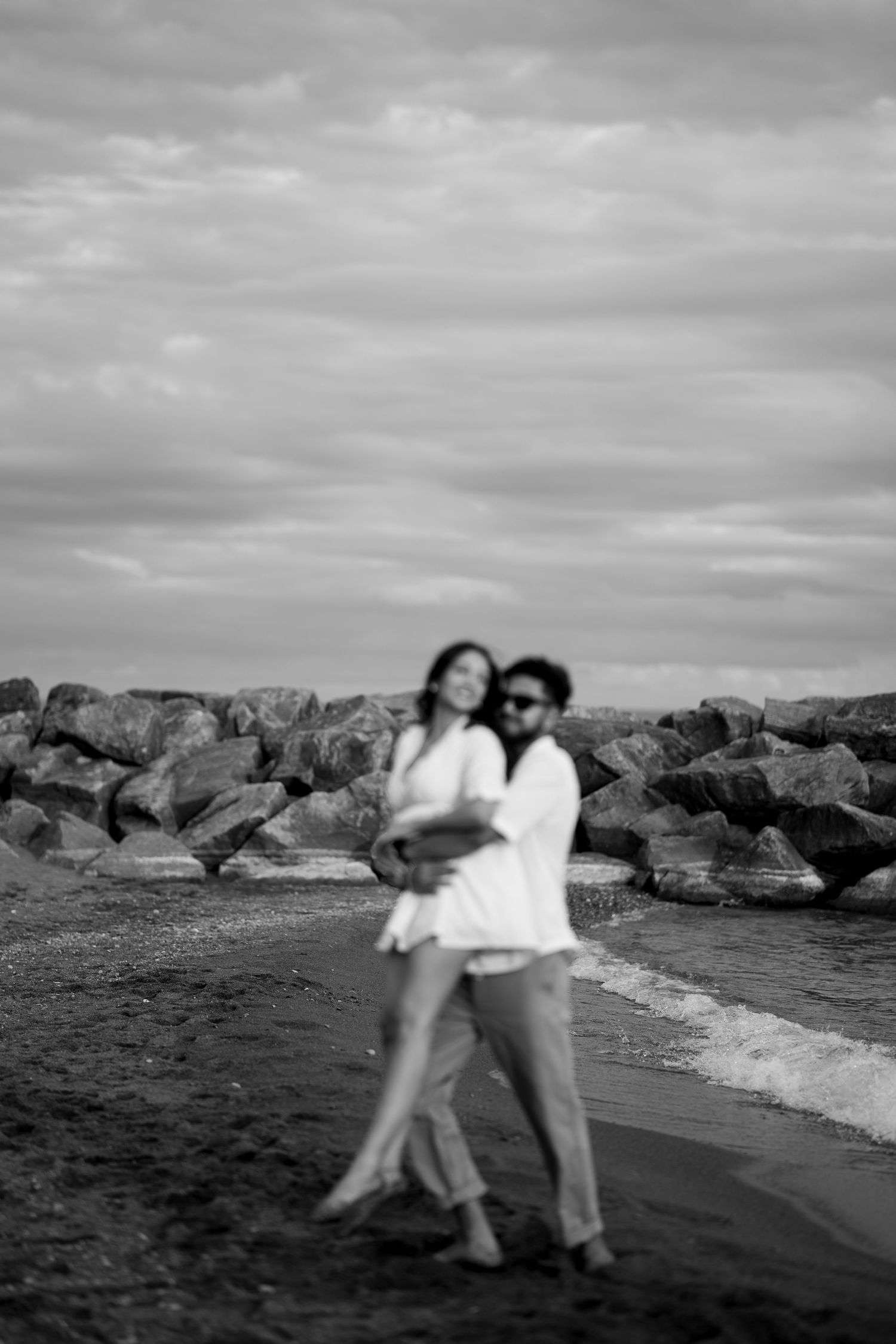 A romantic dance sequence on a rocky beach shore captured in black and white.