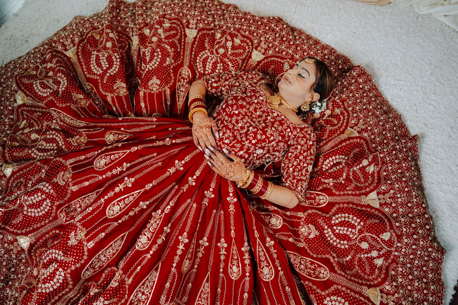 Detailed view of a red bridal lehenga with elaborate gold embroidery spread out on display.