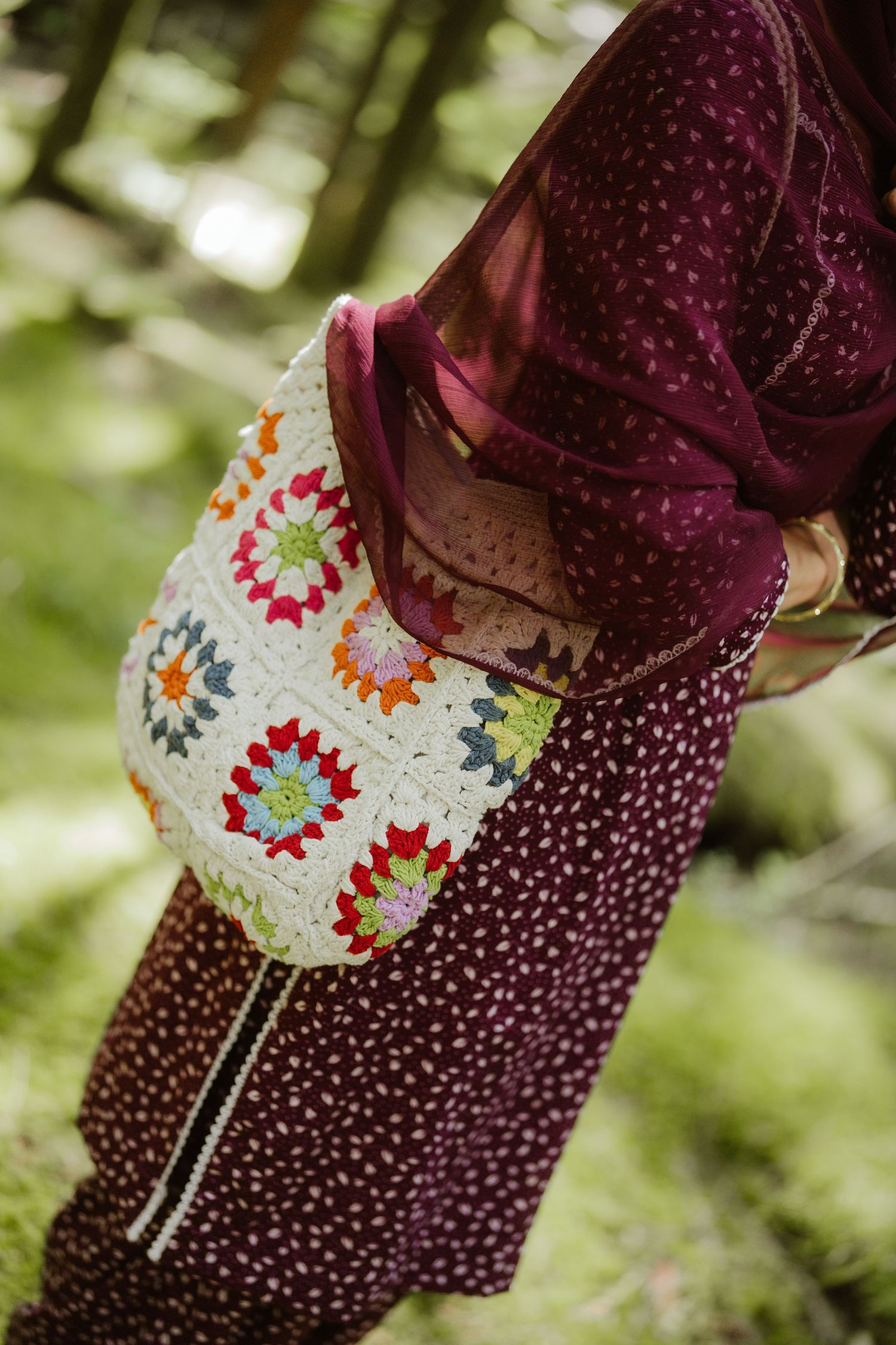 Close-up of colorful crochet granny square bag carried by woman in burgundy Indian ethnic outfit outdoors.