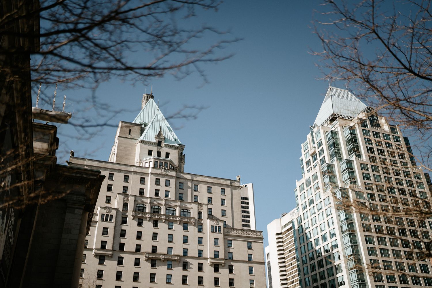 A panoramic view of historic buildings and modern skyscrapers along a city street with bare winter trees.