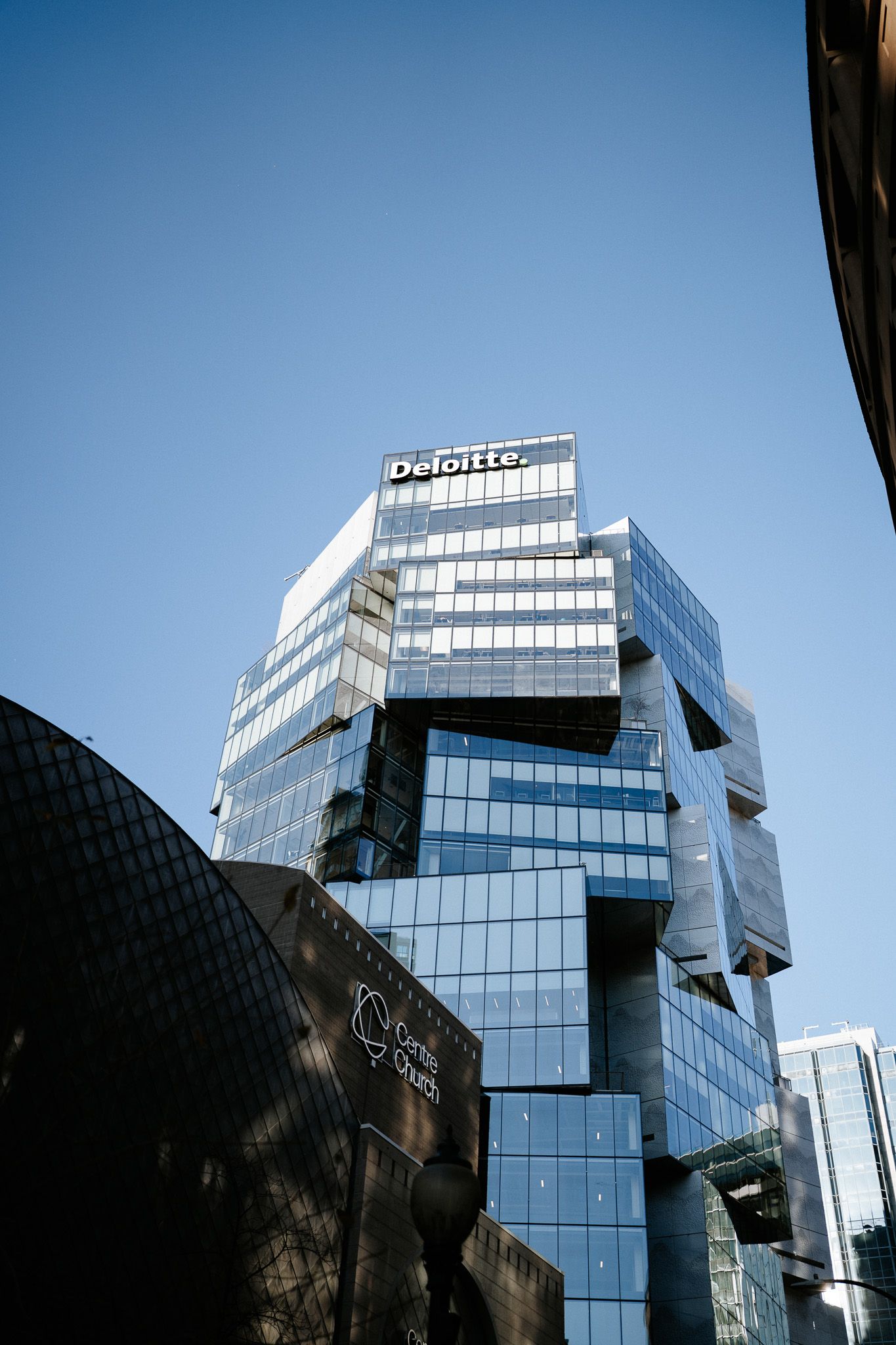 Modern glass office building with reflective windows and angular architecture against blue sky.