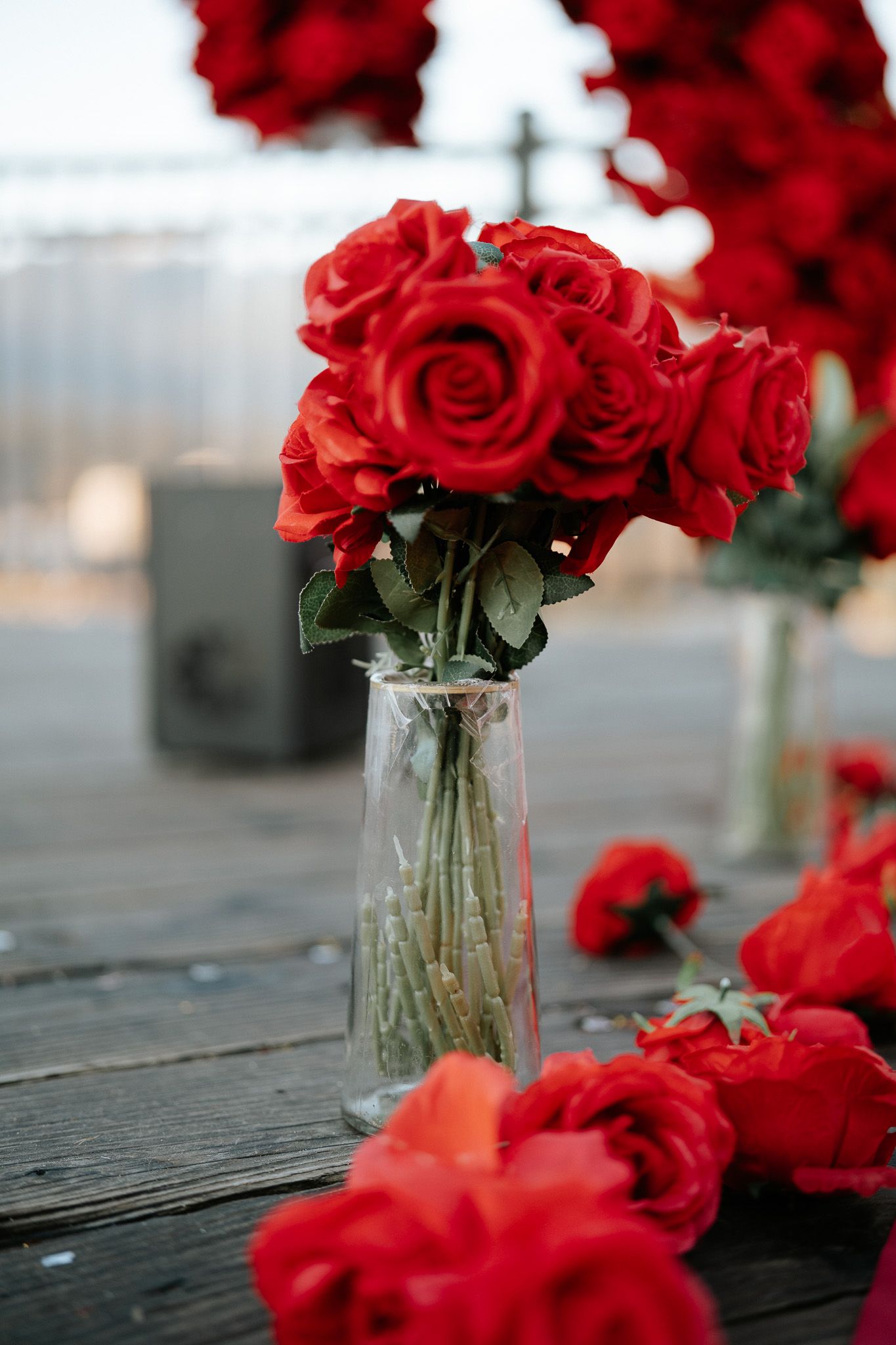Red roses arranged in clear glass vases on a weathered wooden surface create a romantic rustic display.