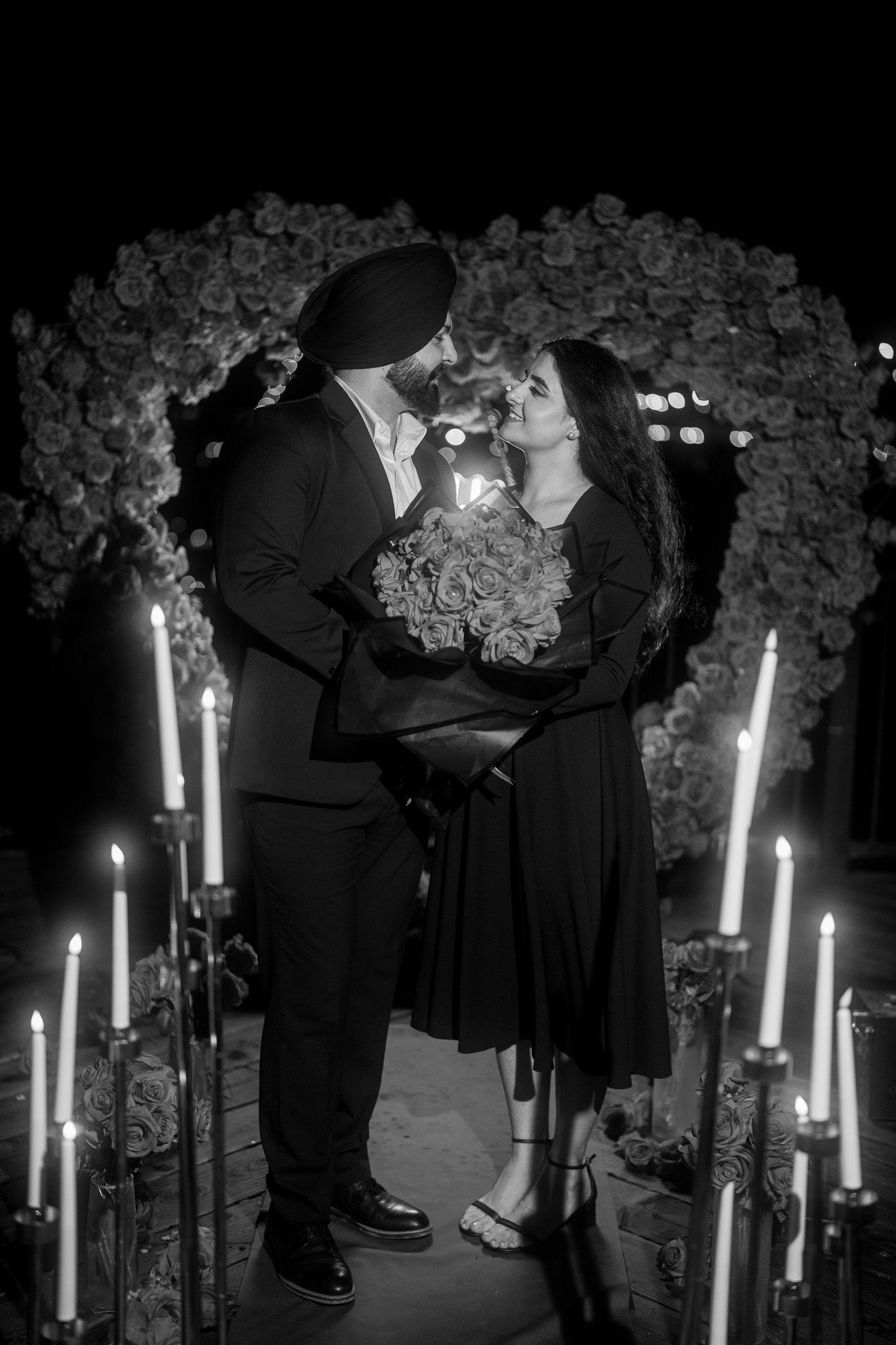 A romantic black and white photo under a floral arch with lit candles creating an intimate atmosphere.